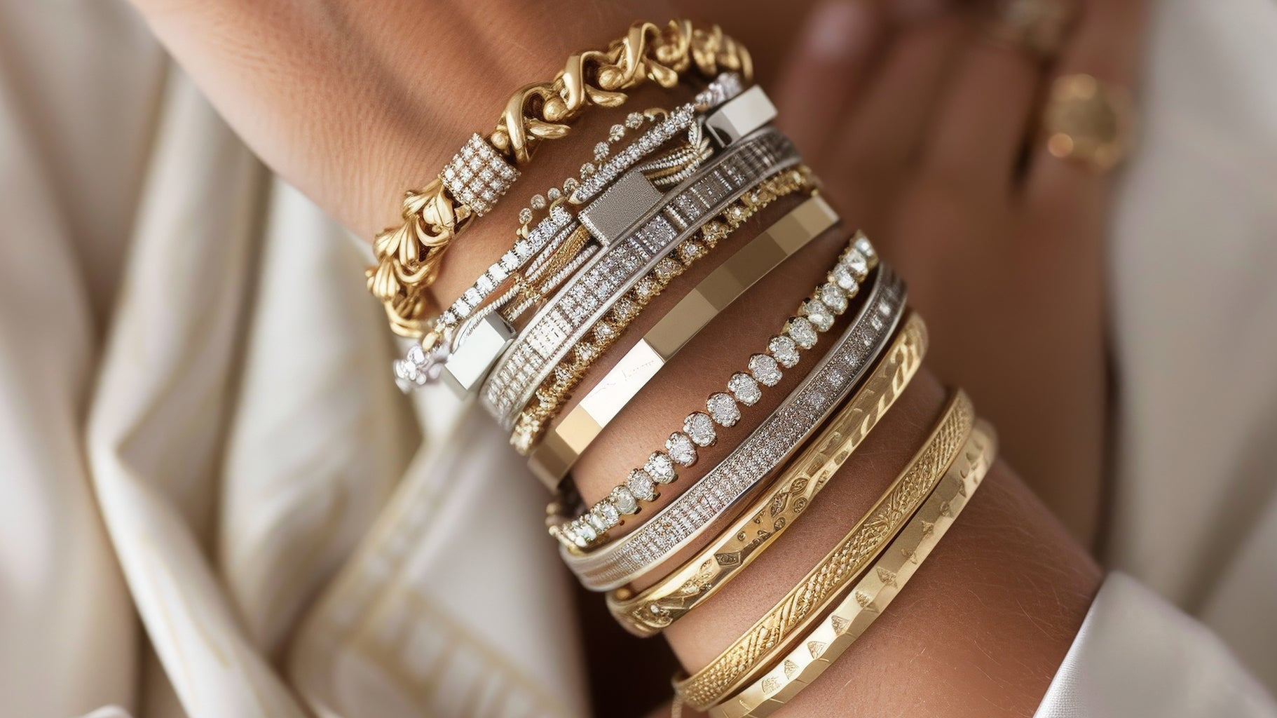 A woman’s wrist stacked with multiple 18K gold-plated bangles, bracelets, and cuffs in stainless steel and brass base, featuring chain links, geometric designs, and diamond-like embellishments — showcasing luxury wrist jewellery styling.
