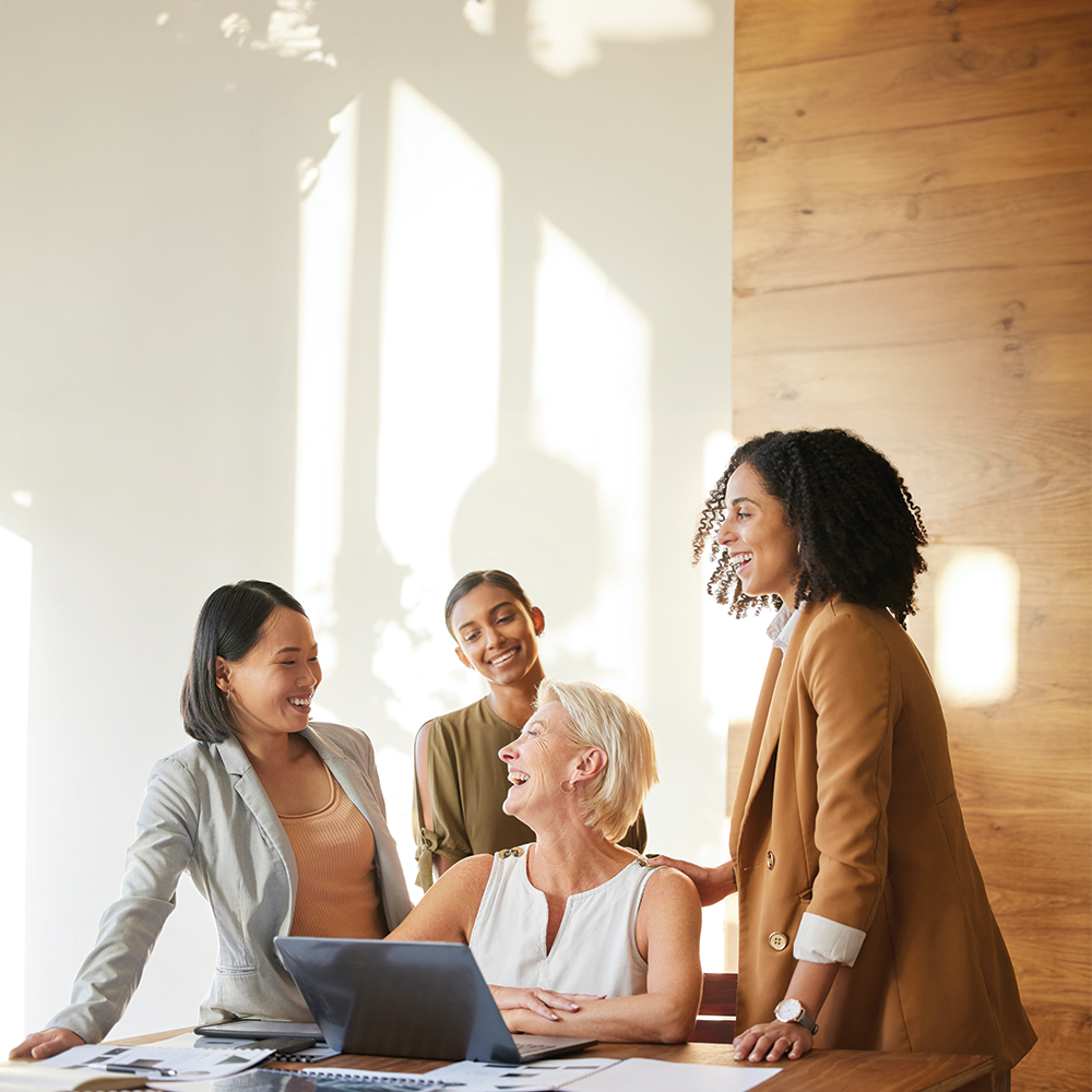 Professional women collaborate on a laptop for a marketing meeting, showcasing teamwork and planning. In the office, managers and employees work on design ideas, fostering collaboration and delivering engaging presentations.