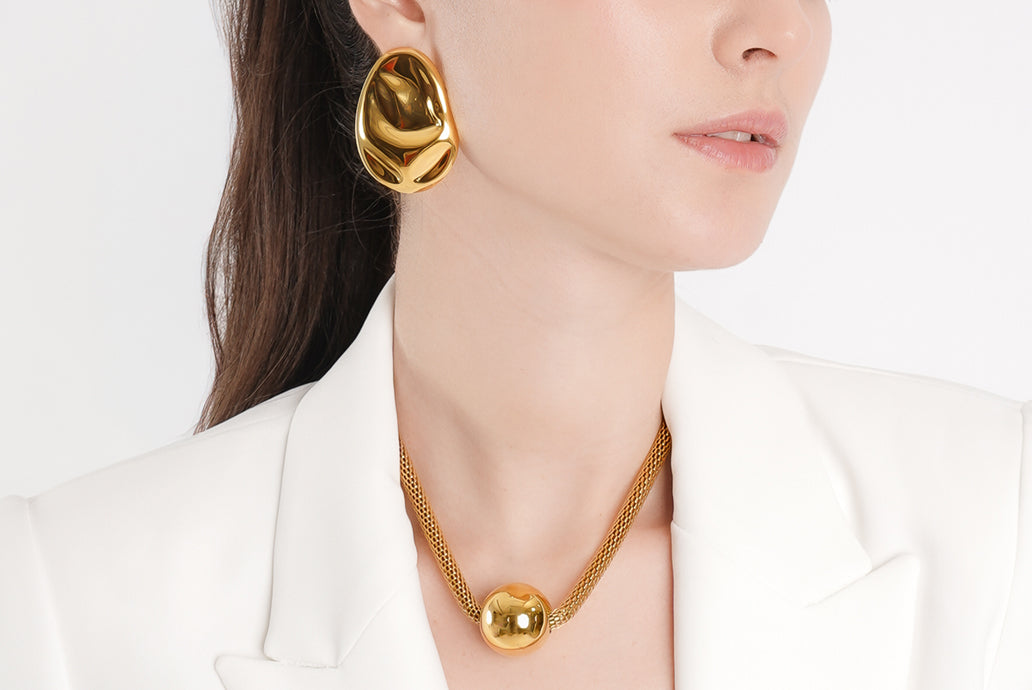 Woman wearing premium demi-fine gold earrings and necklace against a white background