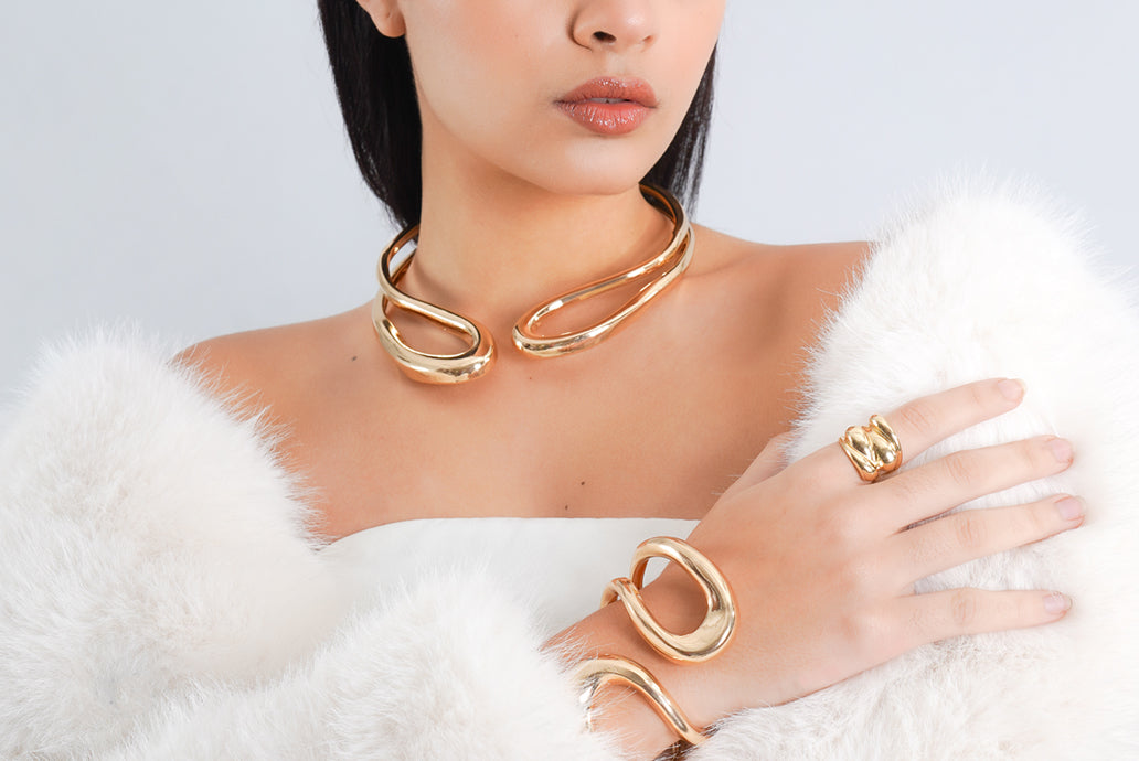 Woman wearing premium demi-fine gold jewellery including a necklace, bracelet, and ring on a white background