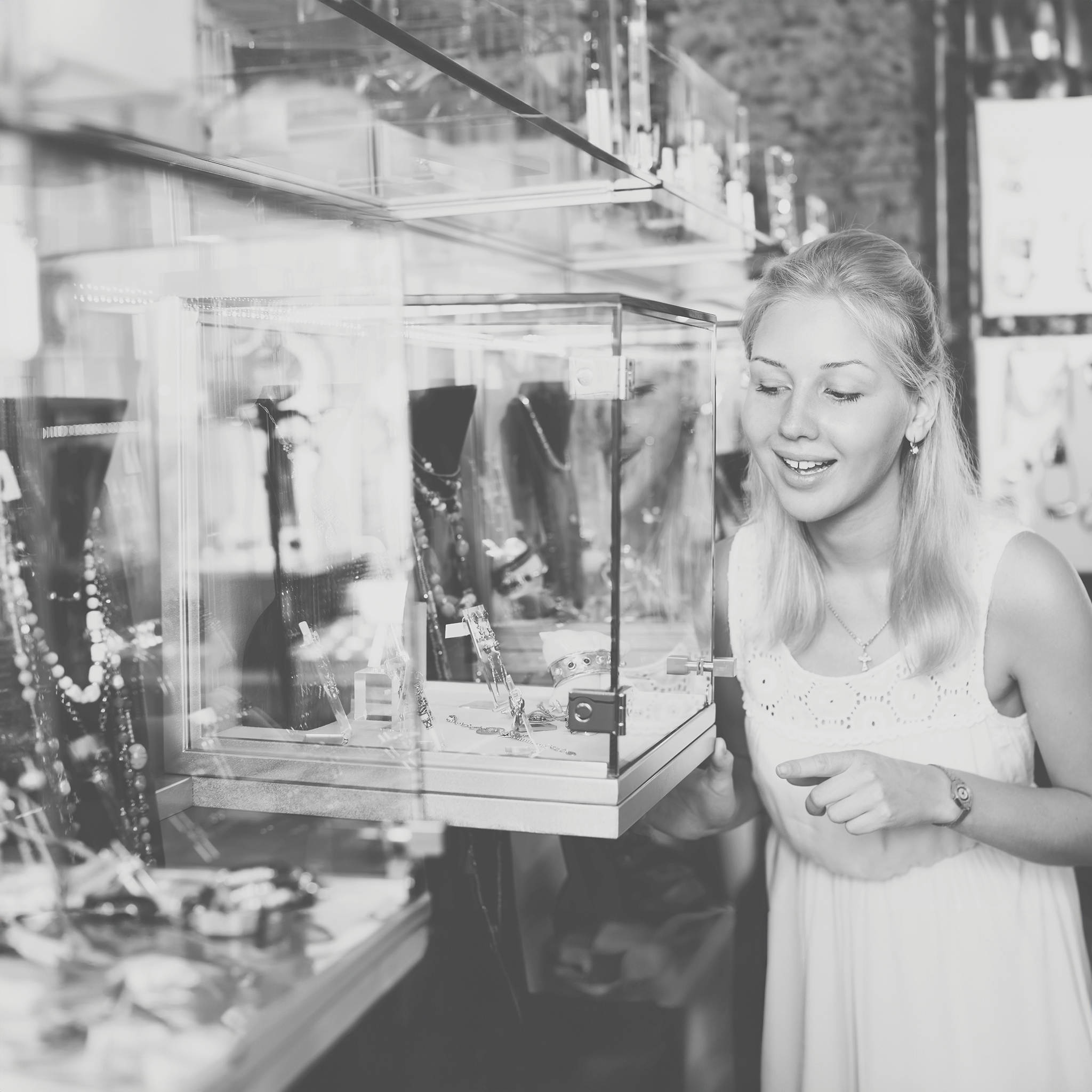 Excited young woman looking at trendy accessories and bijouterie at glass showcase in store.