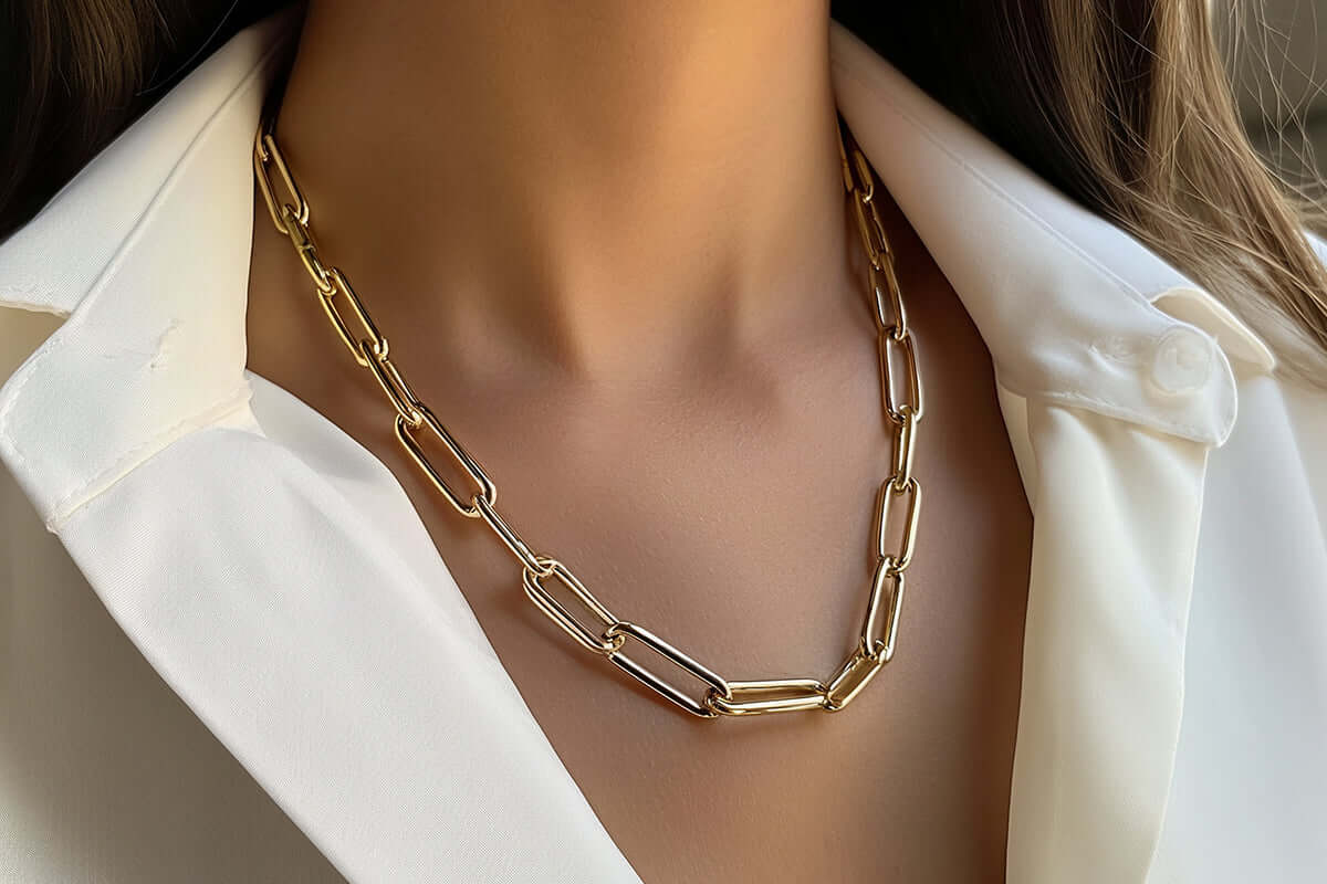 Close-up of a woman's neck wearing a gold chain-link necklace, styled elegantly with a white collared shirt.