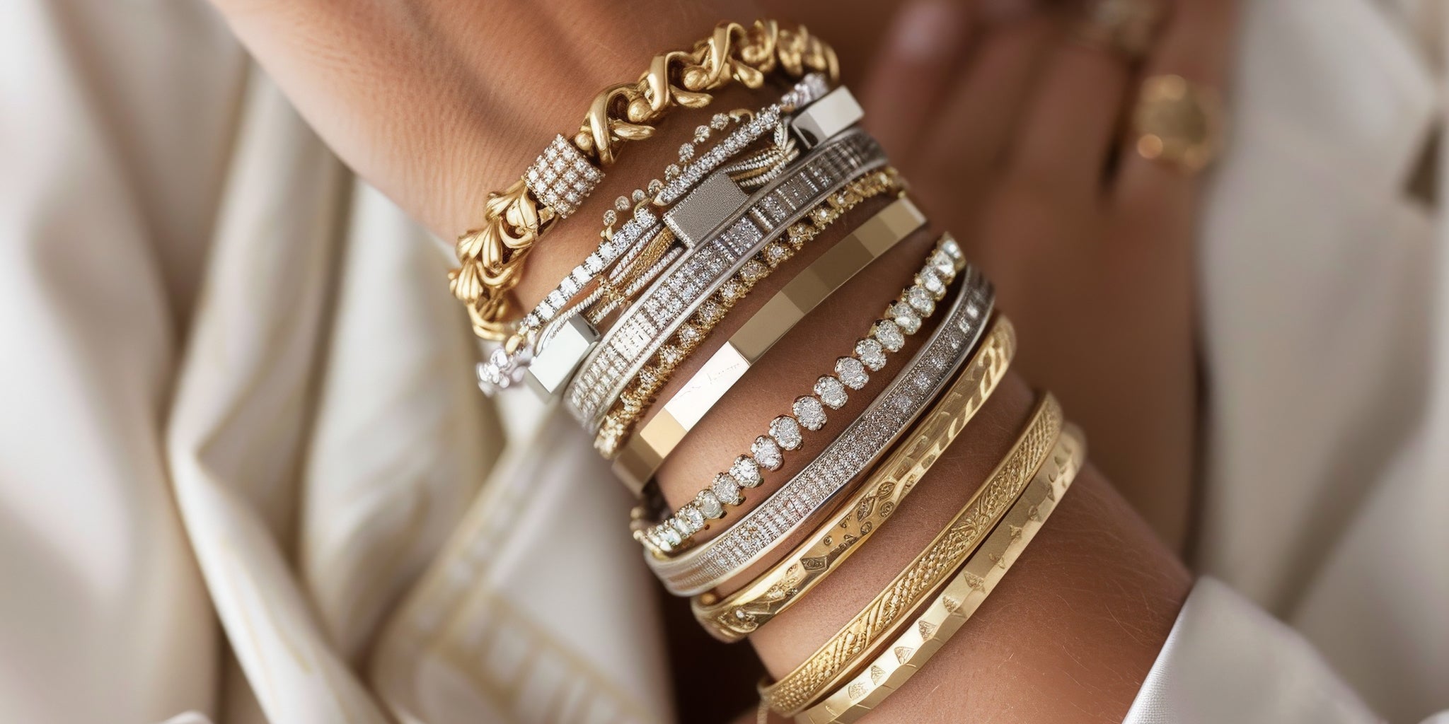 Close-up of a woman's wrist stacked with mixed metal and textured bracelets, featuring gold, silver, and crystal accents, showcasing an elegant, layered look.
