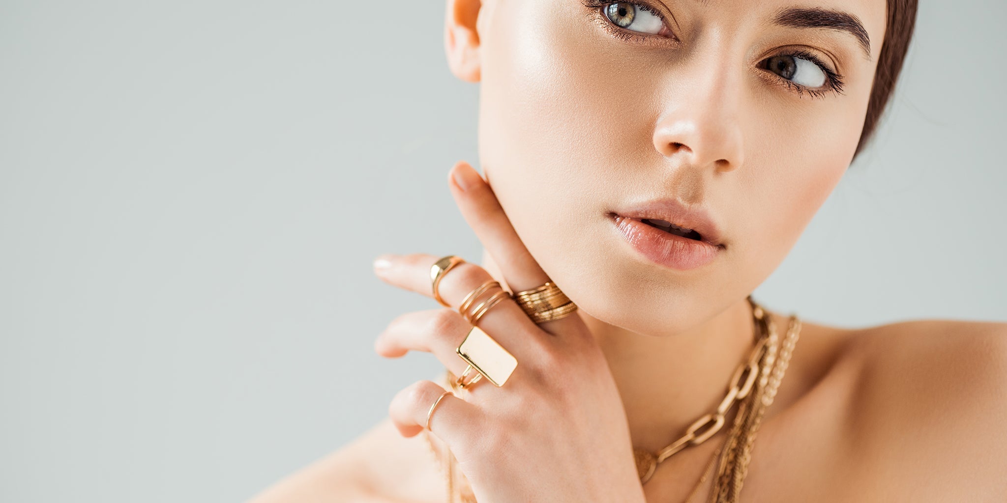 Woman wearing layered gold necklaces and multiple gold rings, showcasing elegant and minimalist jewelry styling.