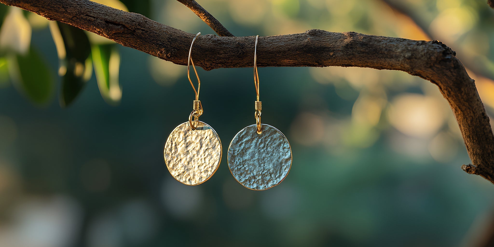 18K gold-plated hammered disc earrings hanging from a tree branch in natural sunlight, reflecting sustainability and nature-inspired jewelry design.
