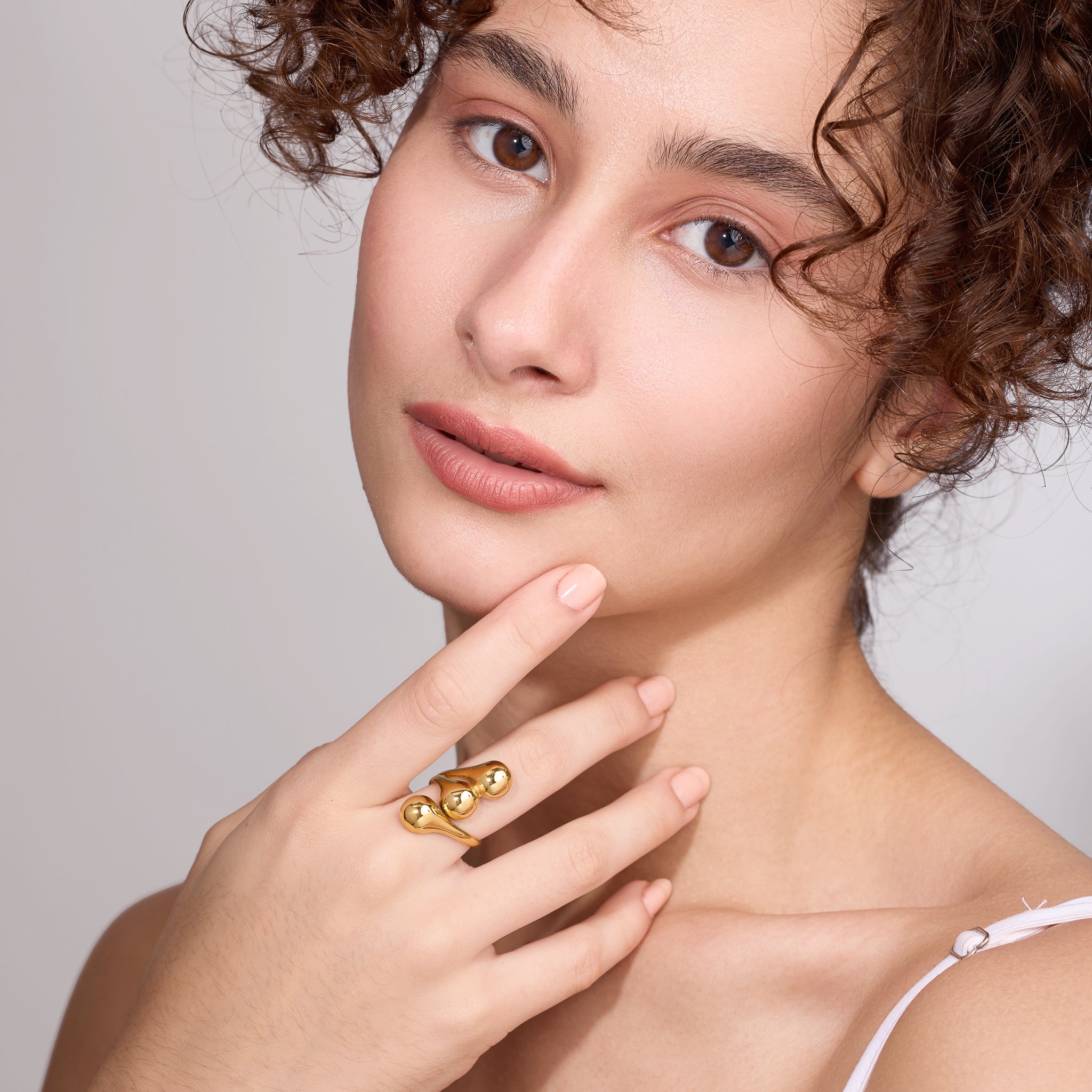 Woman wearing a gold ring on her finger against a neutral background
