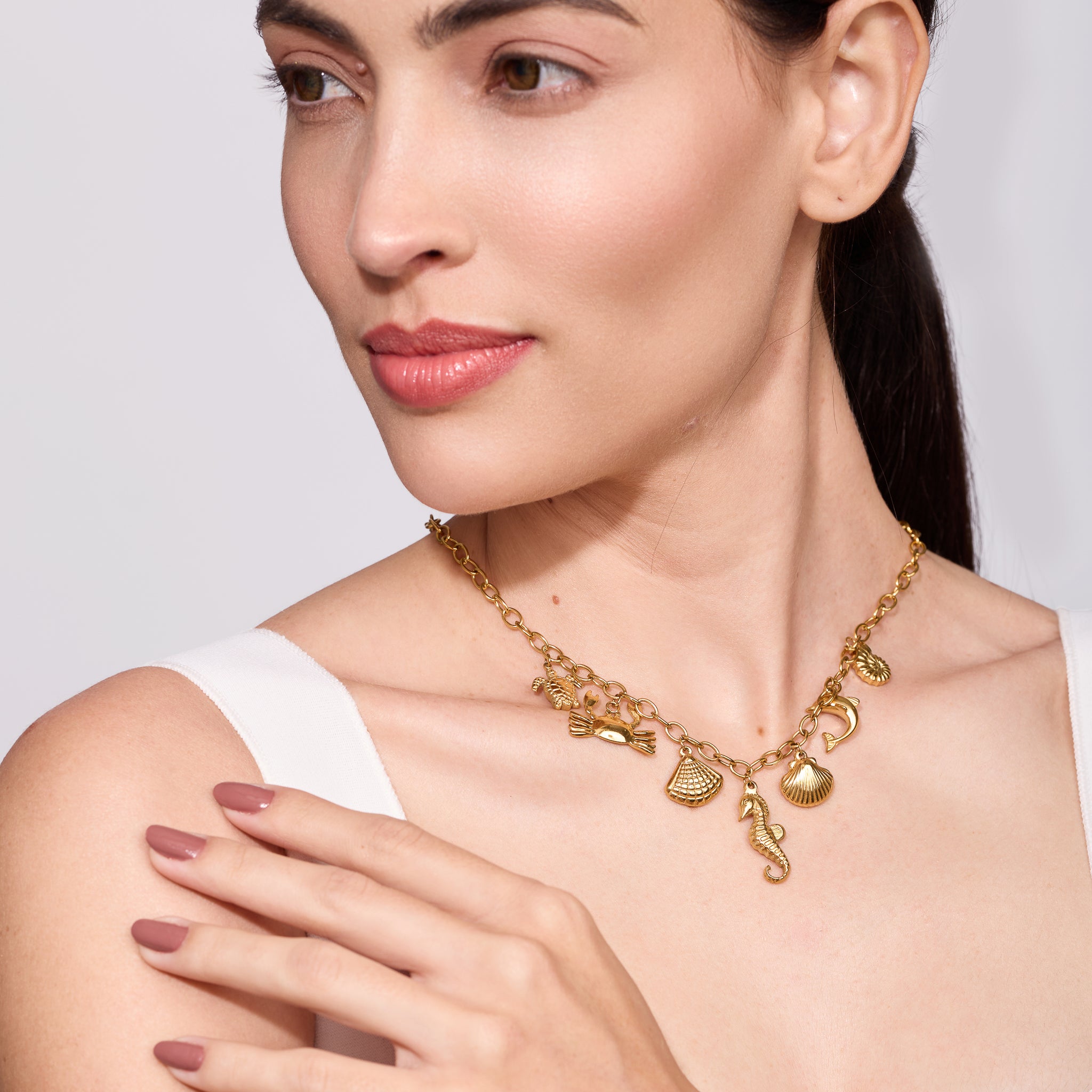 Woman wearing a gold necklace with sea charms on a plain background