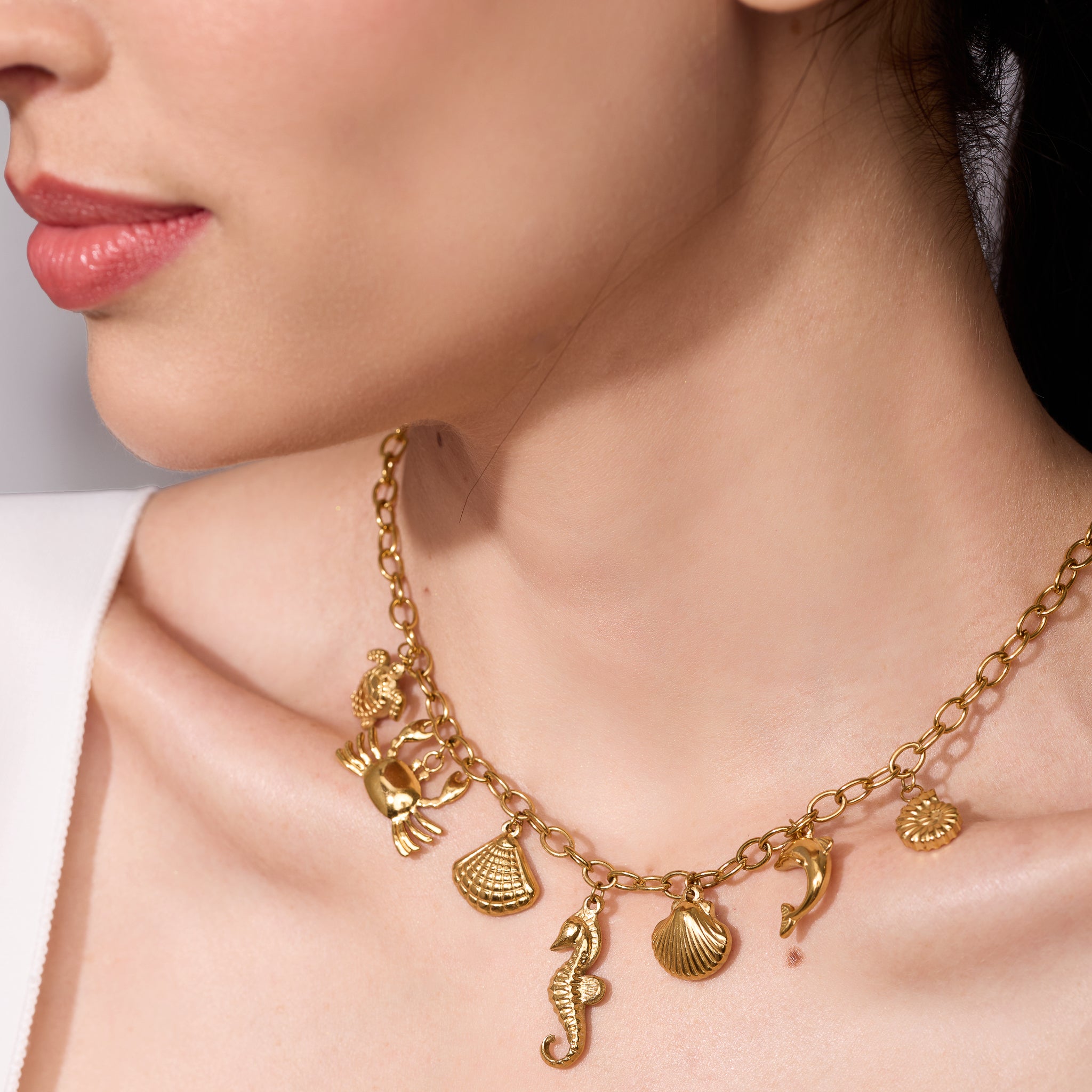 Woman wearing a gold necklace with sea charms on a plain background