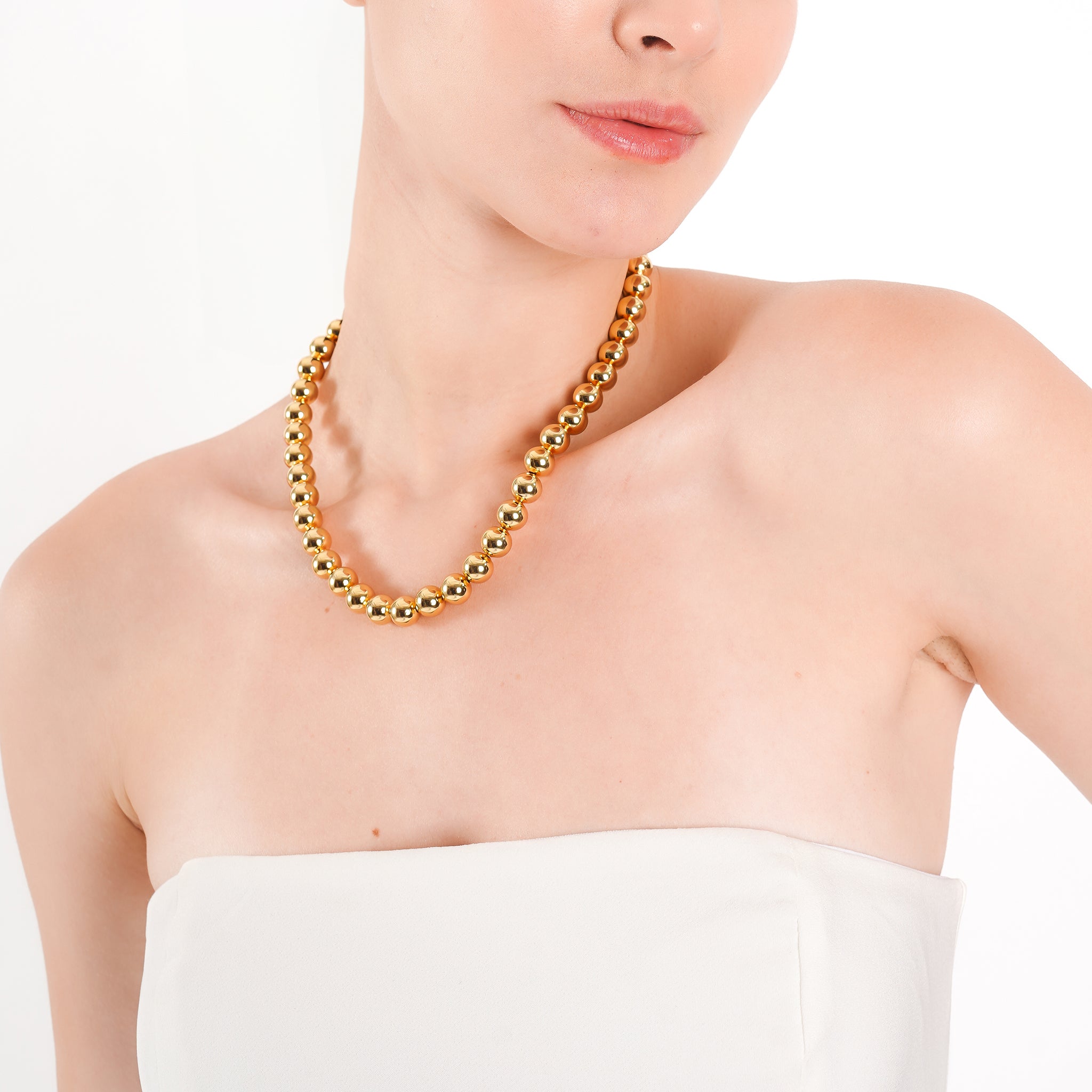 Model wearing an 18K gold-plated ball chain necklace with polished beads, adding a classic touch of elegance to her minimal outfit.