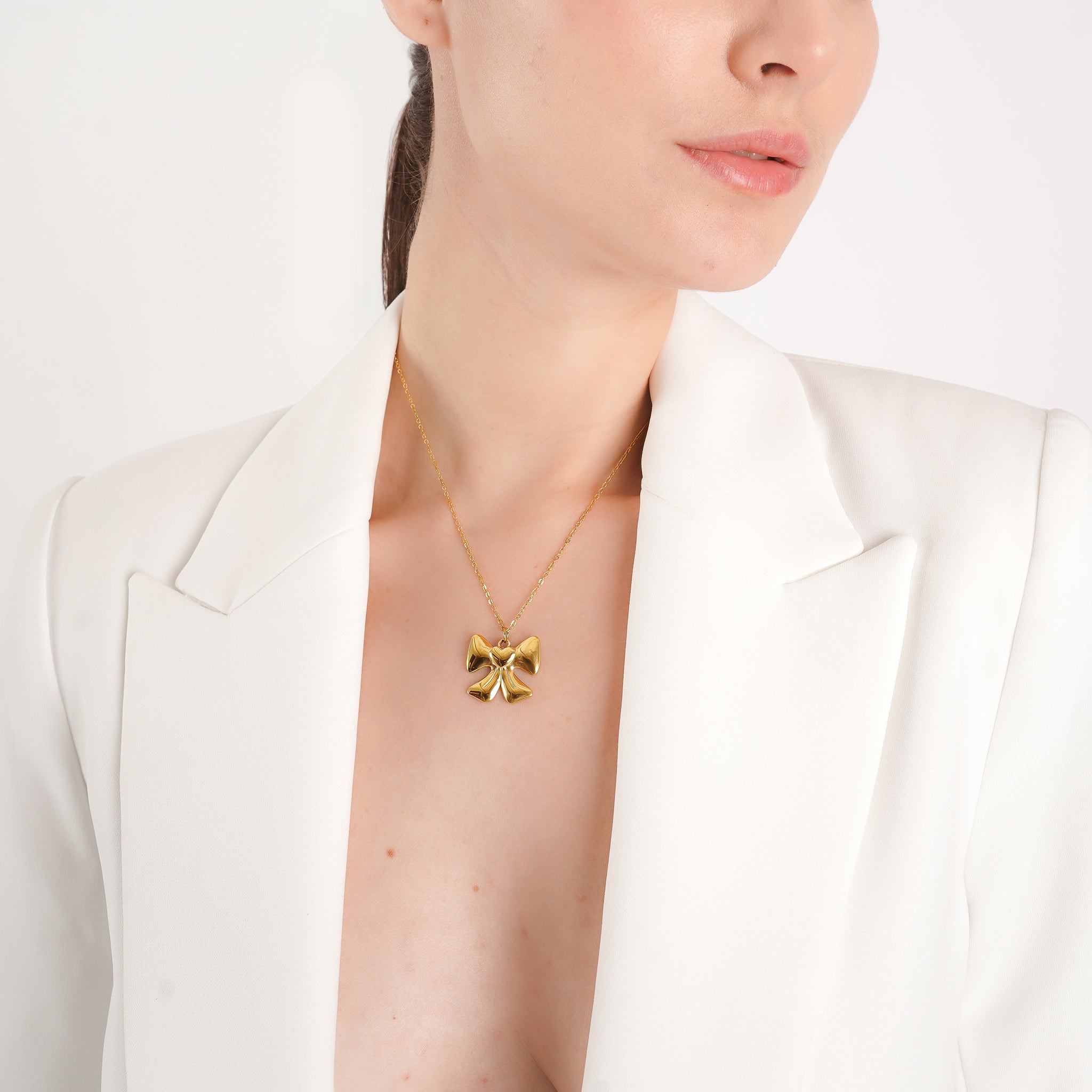 Model wearing an 18K gold-plated necklace with a bow-shaped pendant, adding a playful and elegant accent to her chic outfit.