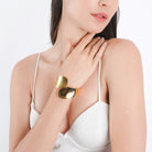A model wearing an 18K gold-plated cuff bracelet with a fluid, curved design, styled elegantly with a minimalist white outfit.
