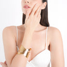 Woman wearing an 18K gold-plated crisscross cuff bracelet, styled with a sleeveless white top, showcasing its bold, polished finish and modern design.