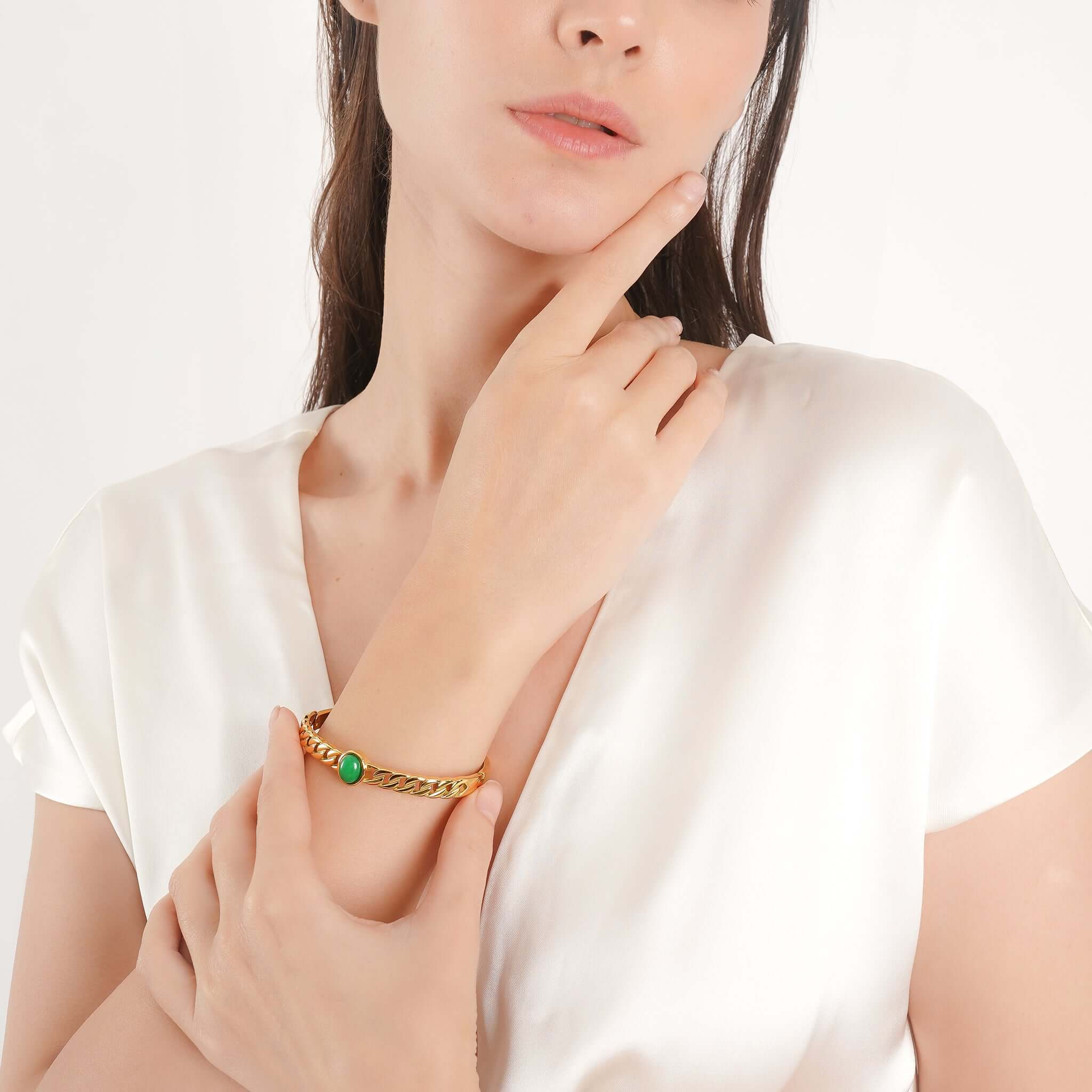 Woman wearing the gold-plated chain bangle with a green stone, elegantly styled on her wrist, complementing her minimalist white outfit.