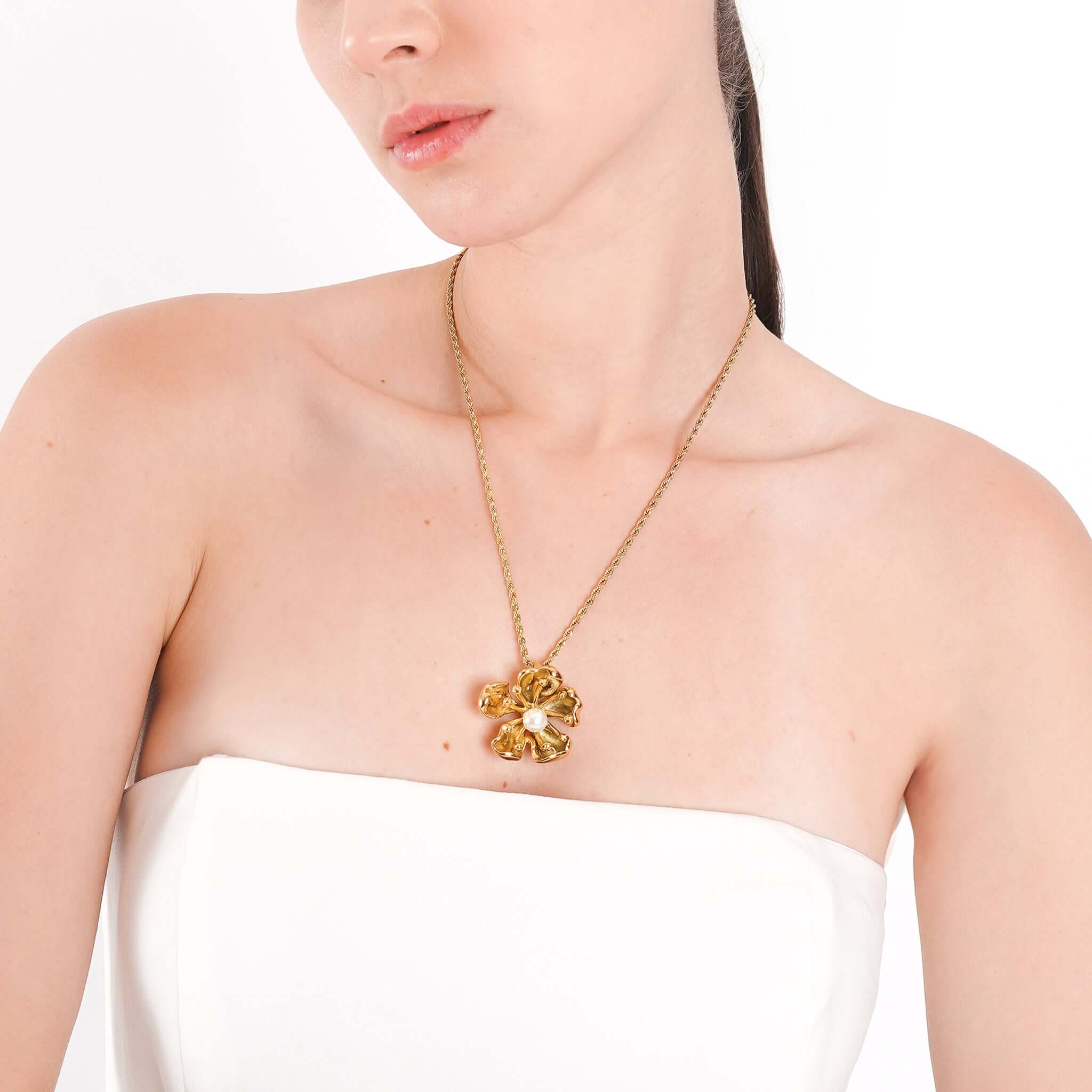 A model showcasing the 18K gold-plated floral necklace, with its central pearl resting elegantly against her upper chest, highlighting the intricate design.