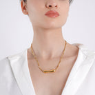 Woman wearing the 18K gold-plated necklace featuring a sleek curved bar pendant, adding a touch of minimal elegance to her outfit.