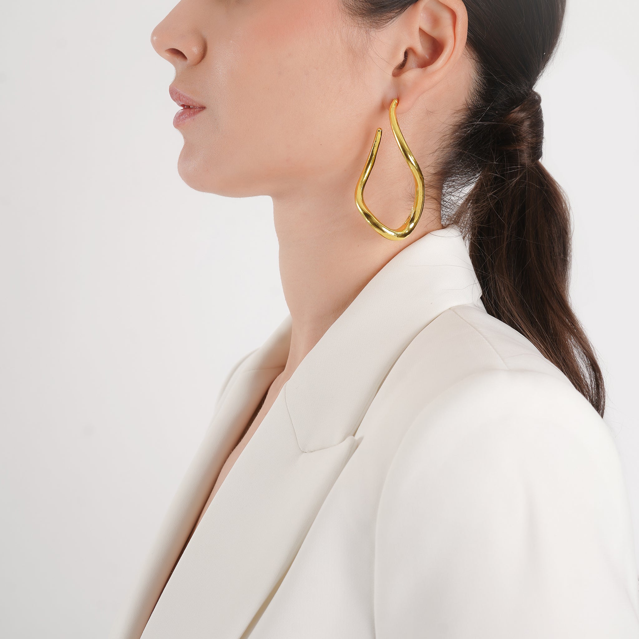 Woman wearing 18K gold-plated abstract twisted hoop earrings, showcasing their fluid and artistic shape complementing her outfit.