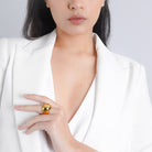 A woman in a white blazer showcasing a gold-plated dome ring on her finger, exuding sophistication and minimalist elegance.