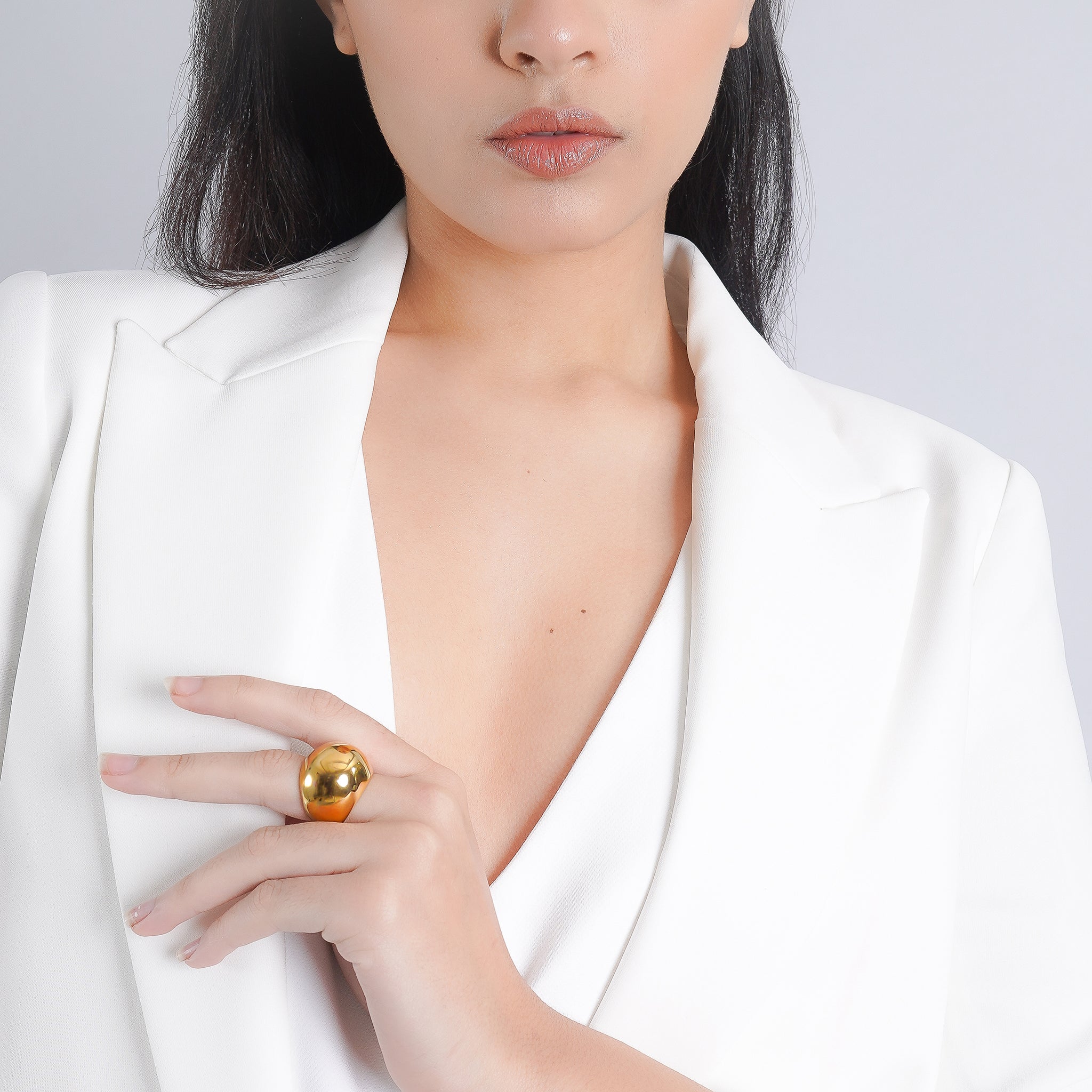 A woman in a white blazer showcasing a gold-plated dome ring on her finger, exuding sophistication and minimalist elegance.