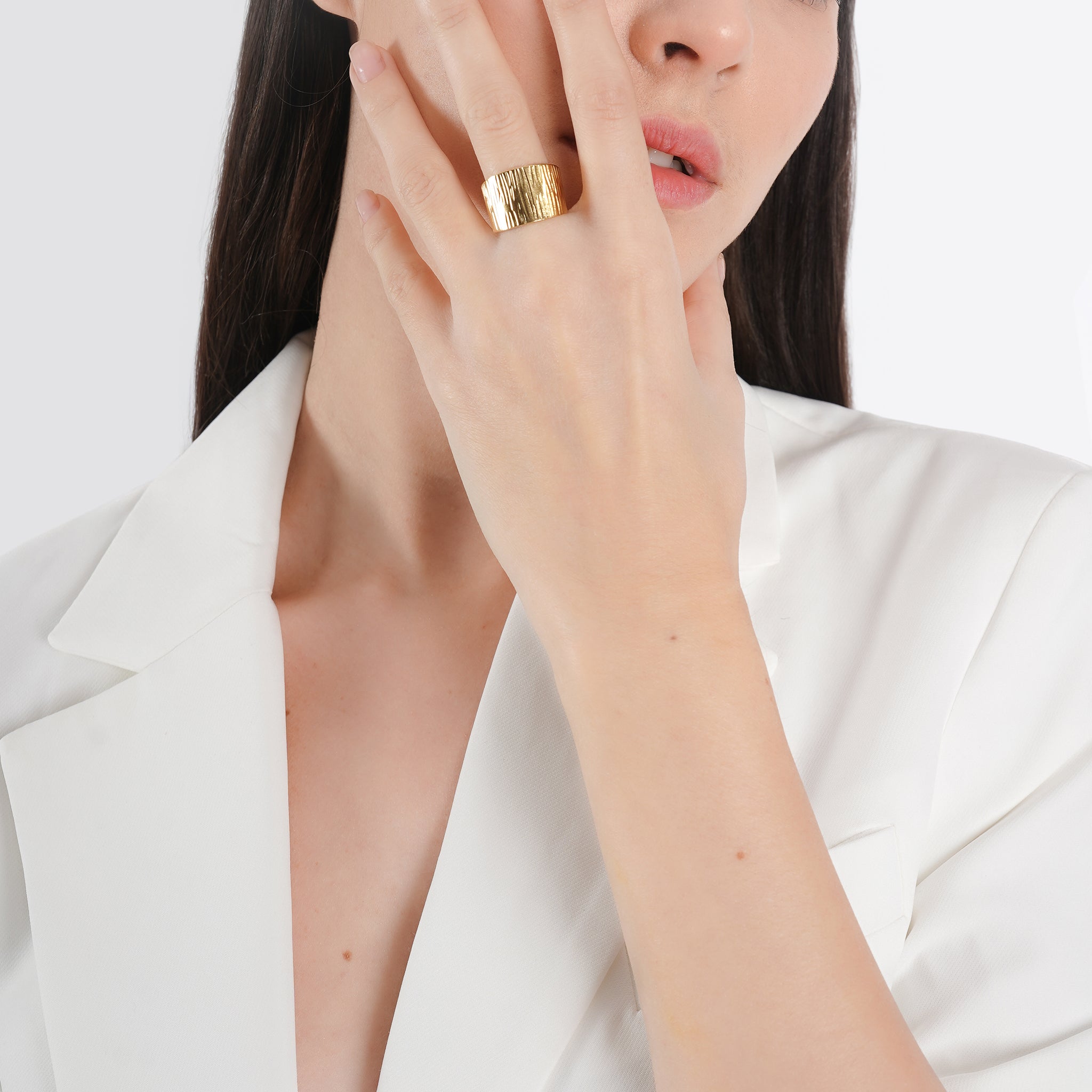 A model wearing the 18k gold-plated textured wide band ring, showcasing its bold and luxurious statement against a chic white outfit.