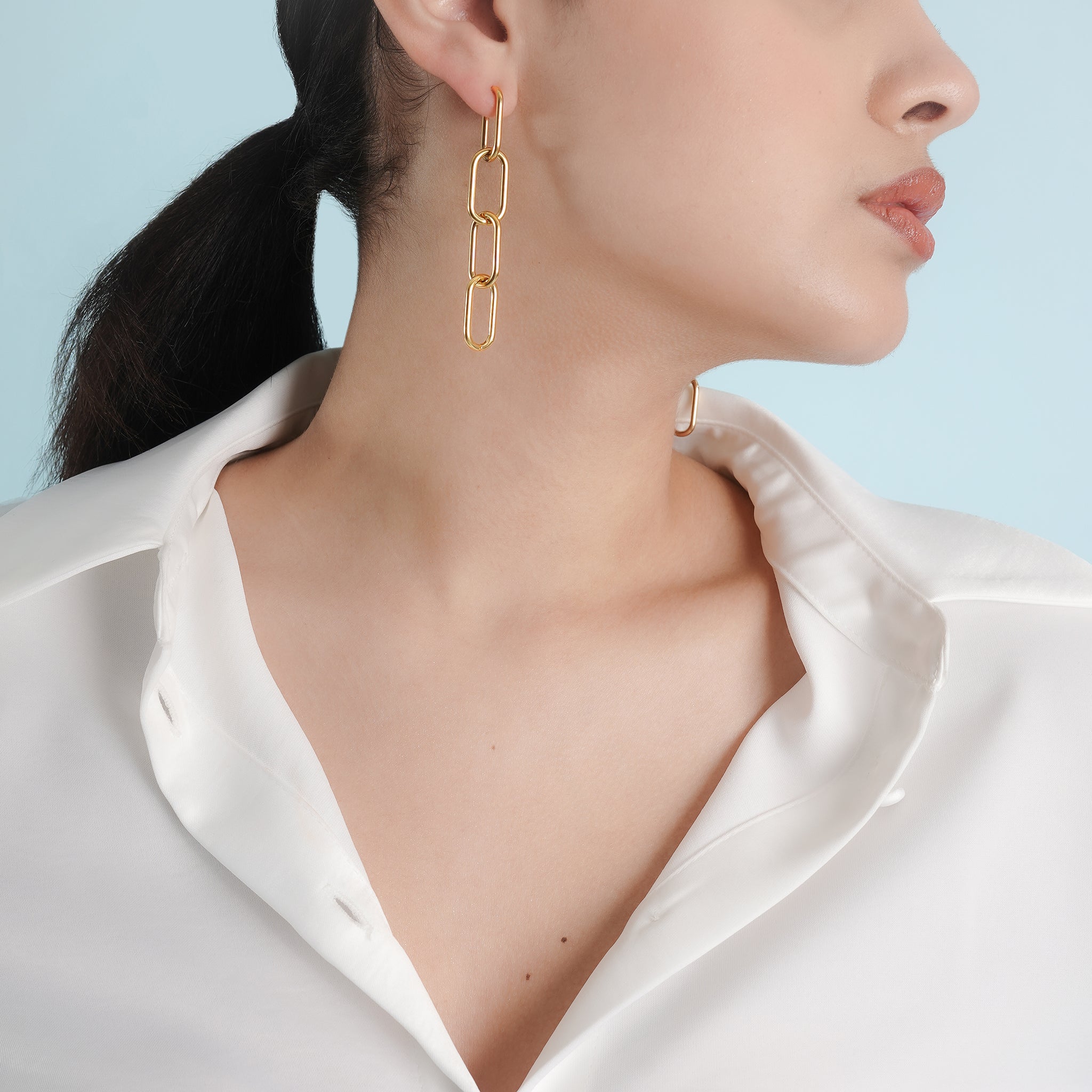 Woman wearing minimalist 18K gold-plated chain drop earrings with interlinked oval links, complementing her white blouse and refined style.