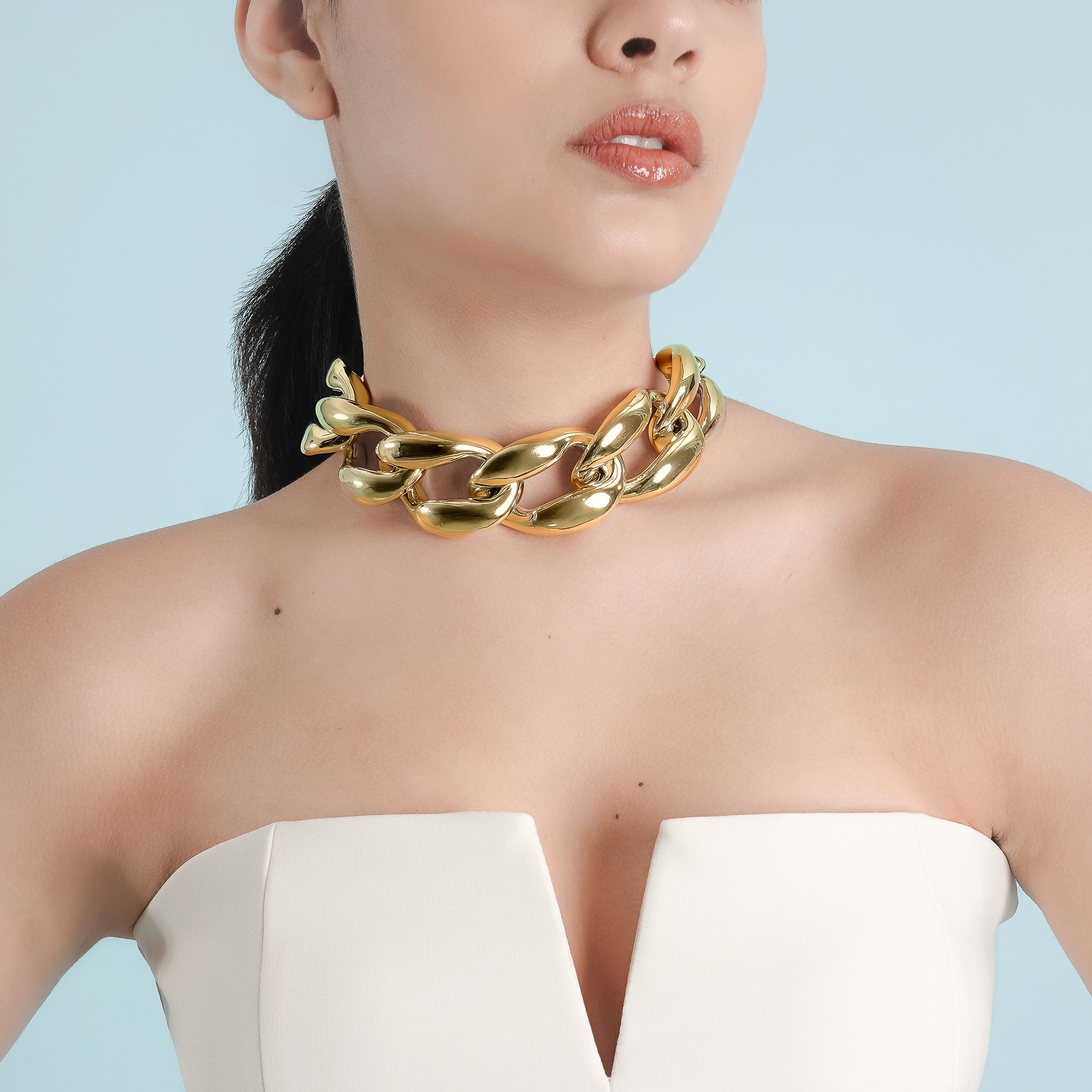 Model wearing an gold-plated chunky chain link choker, paired with a strapless white dress, showcasing its statement design against smooth skin.