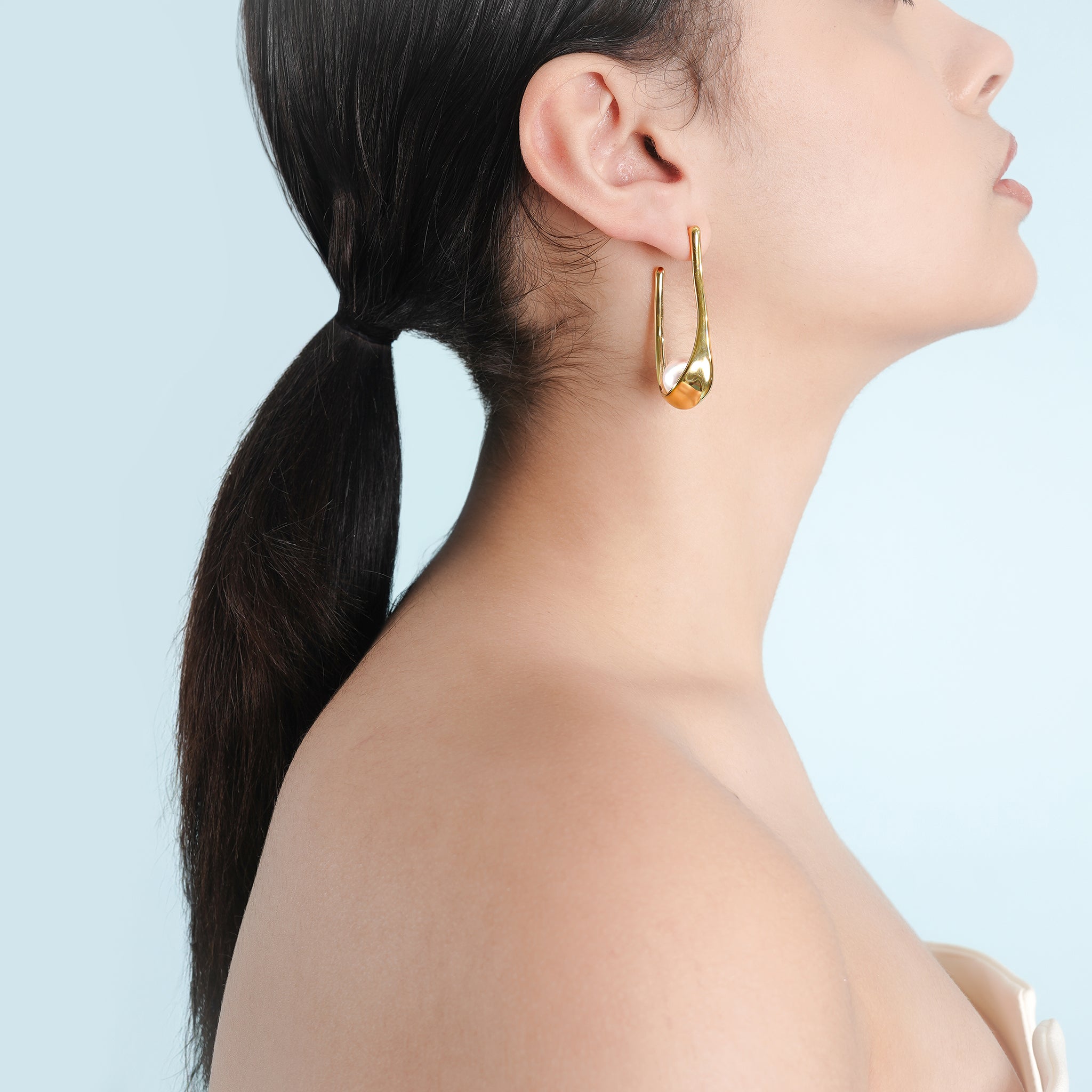 Model wearing the 18K gold-plated drop earrings with pearl detailing, styled with a sleek ponytail and a minimal strapless top, highlighting their sophisticated, modern charm and graceful drop silhouette.