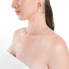 Model wearing 18K gold-plated sculptural earrings with dangling pearls, styled with a strapless white outfit, adding a touch of modern elegance and refined charm.