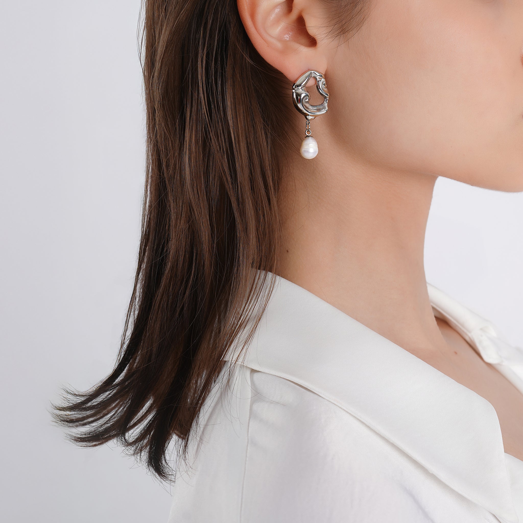 Model wearing silver plated sculptural earrings with dangling pearls, styled with a strapless white outfit, adding a touch of modern elegance and refined charm.