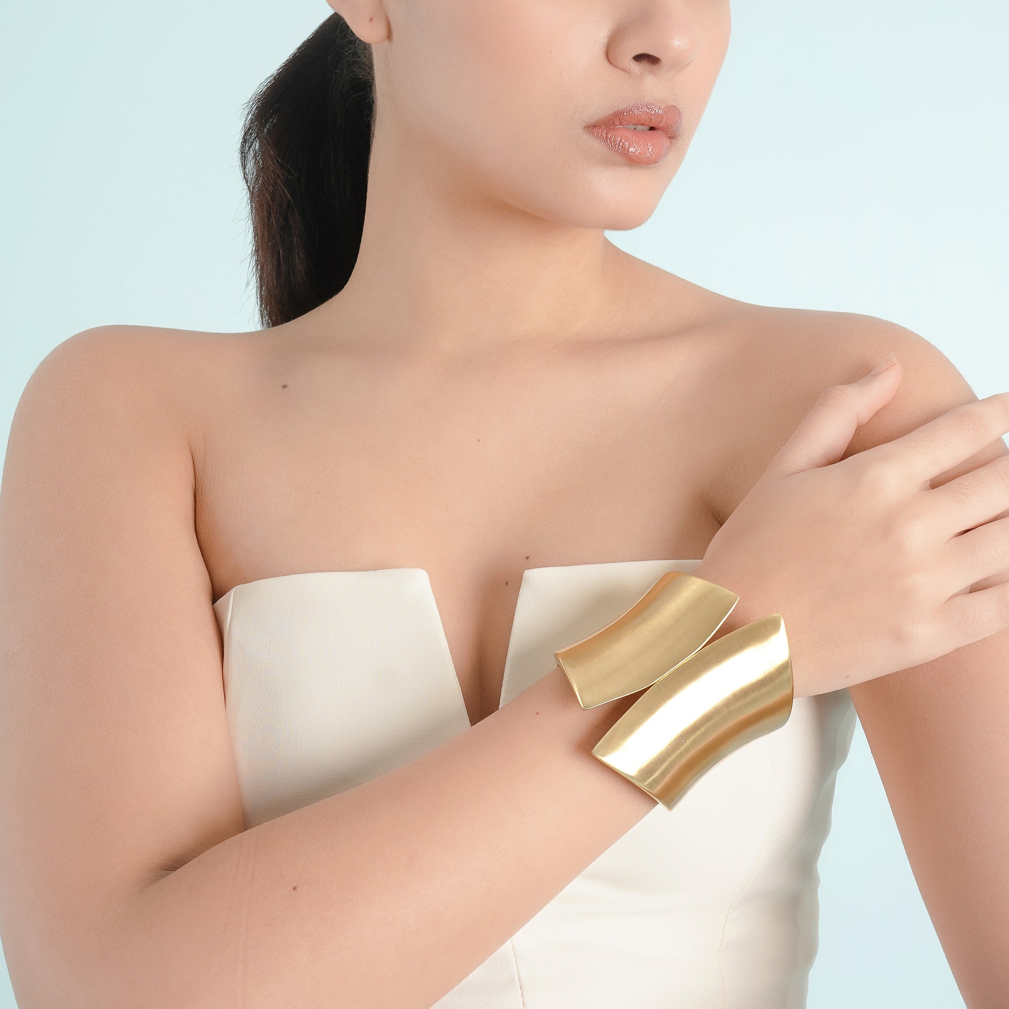 Model wearing an 18K gold open cuff bracelet with a bold, curved design, styled elegantly against a white strapless top.