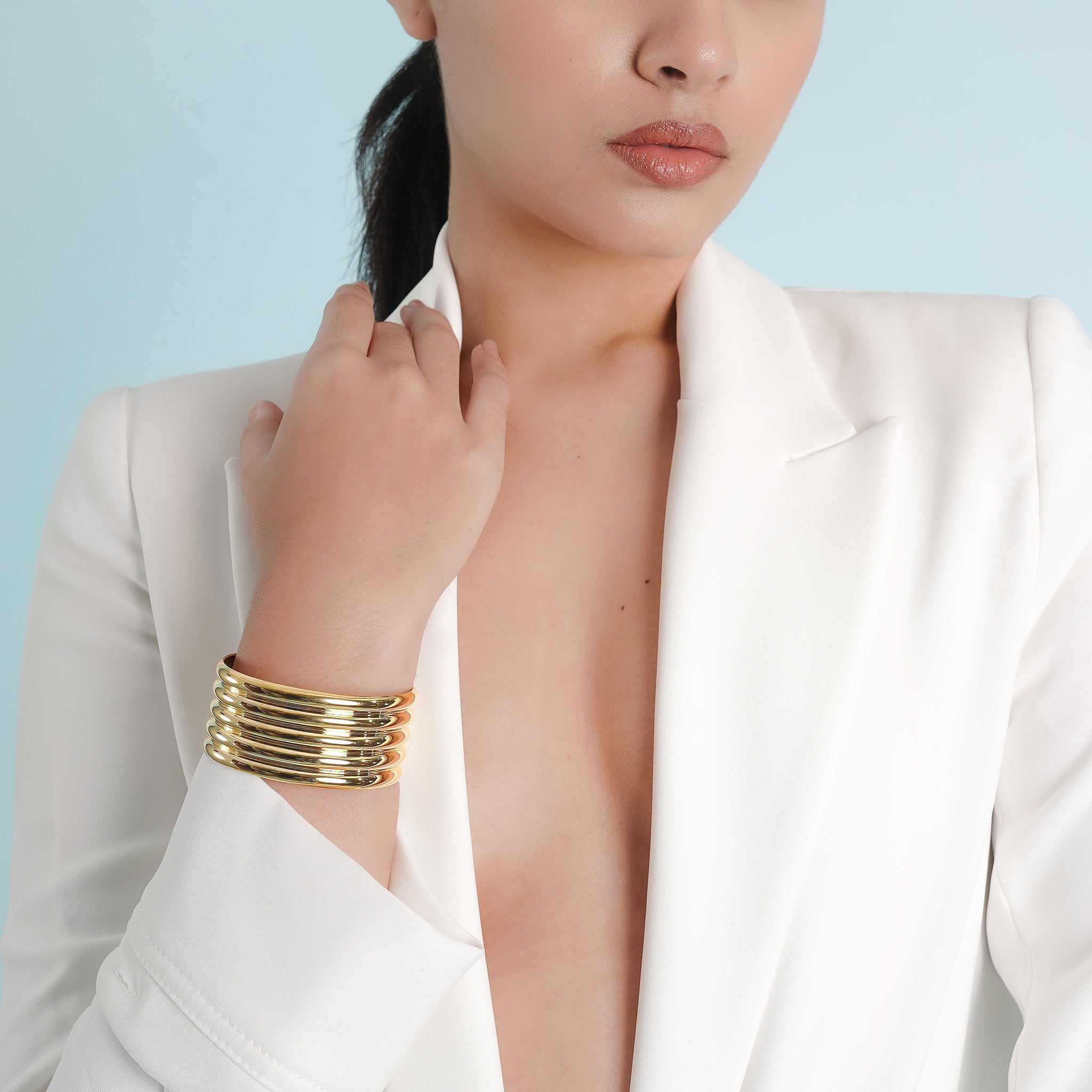 A model wearing the 18K gold-plated ribbed cuff bracelet, paired with a white blazer, showcasing its bold and luxurious appeal on the wrist against a minimal, sophisticated backdrop.
