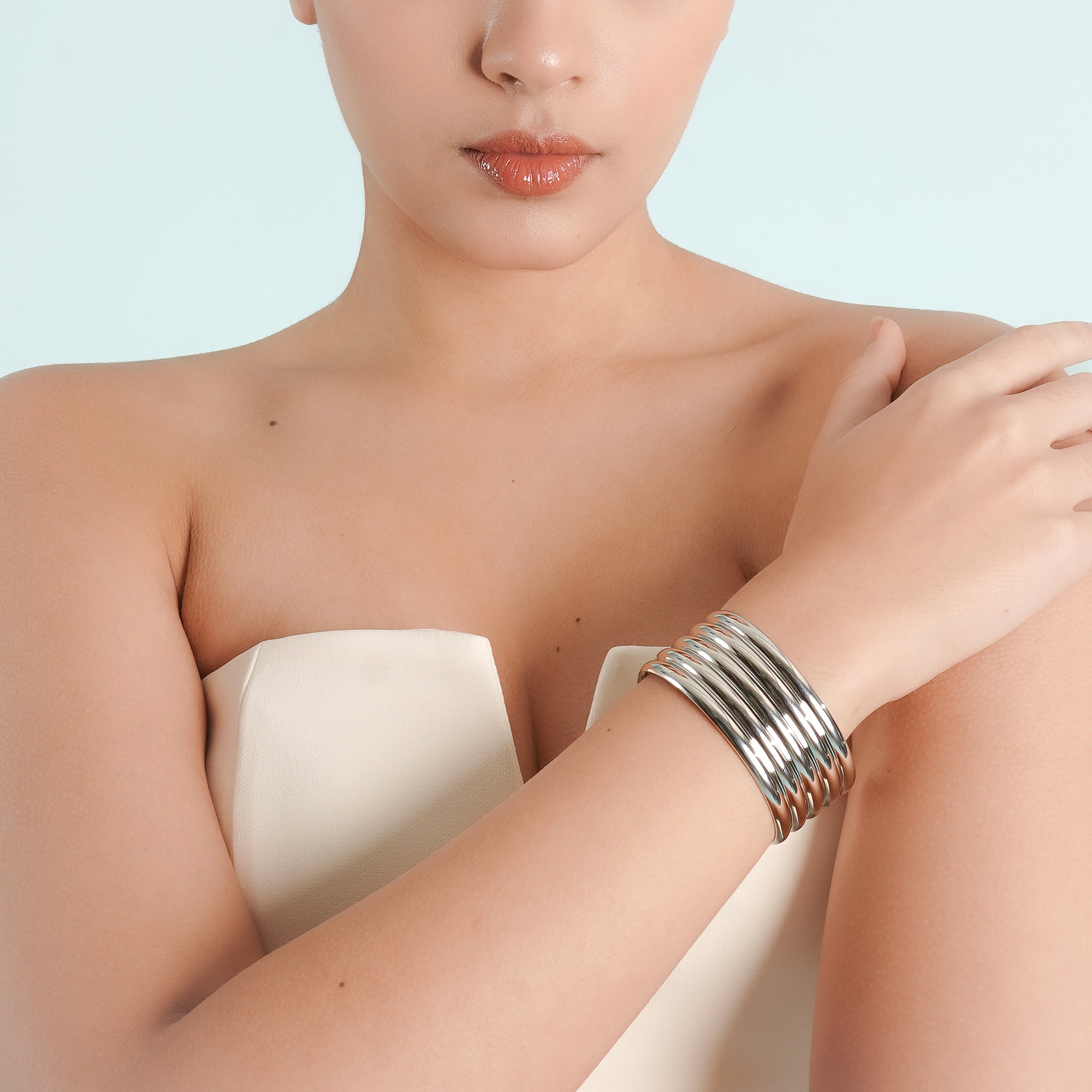 A model wearing the silver plated ribbed cuff bracelet, paired with a white blazer, showcasing its bold and luxurious appeal on the wrist against a minimal, sophisticated backdrop.