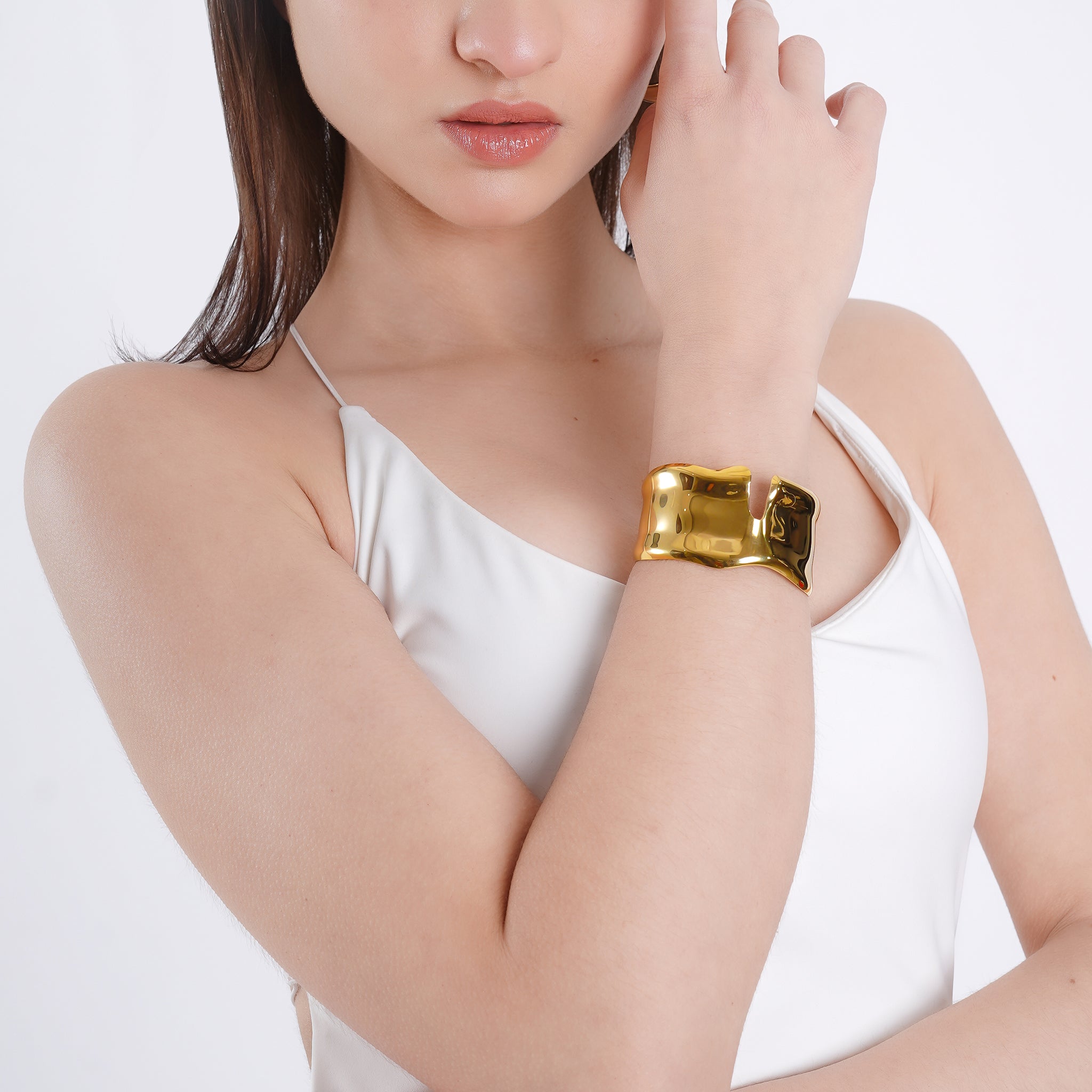 Model wearing an 18K gold-plated open cuff bracelet with a fluid, high-shine design, styled against a white outfit for a refined, elegant look.