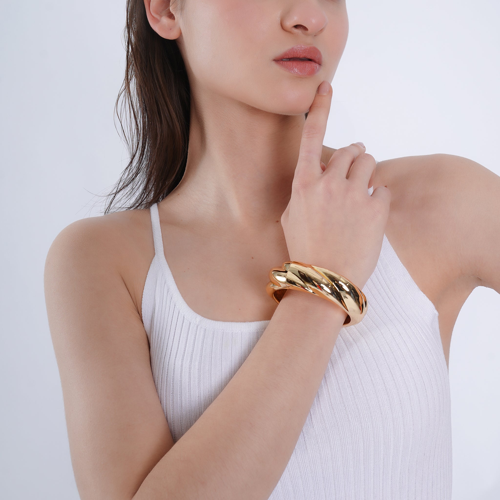 Model wearing an gold-plated twisted bangle with a braided design, styled with a white ribbed tank top for a chic, modern look.