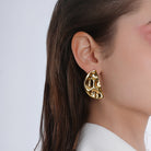 Model wearing a pair of gold-plated abstract half-moon earrings, showcasing their bold, sculptural detailing against a clean, elegant look.