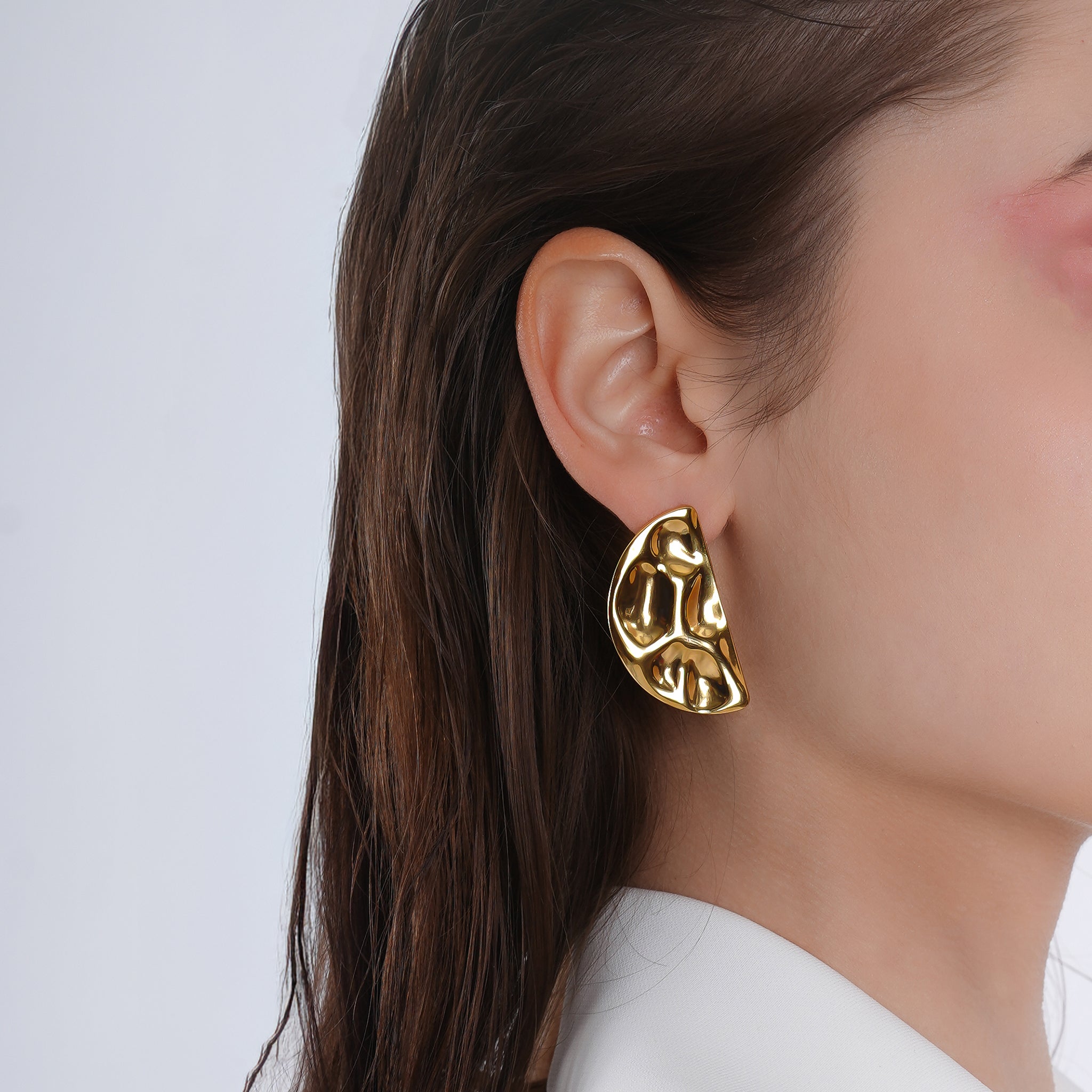 Model wearing a pair of gold-plated abstract half-moon earrings, showcasing their bold, sculptural detailing against a clean, elegant look.
