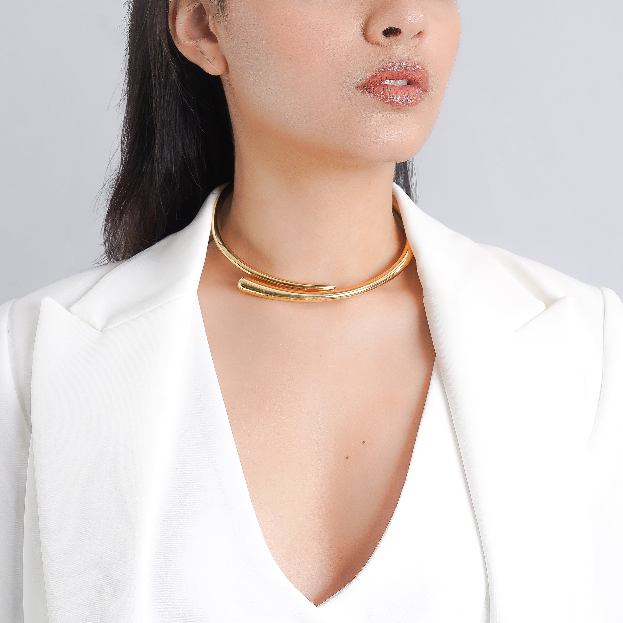 Model wearing an gold-plated minimalist choker necklace with a sleek, curved design, paired with a white blazer, highlighting its modern elegance and simplicity.