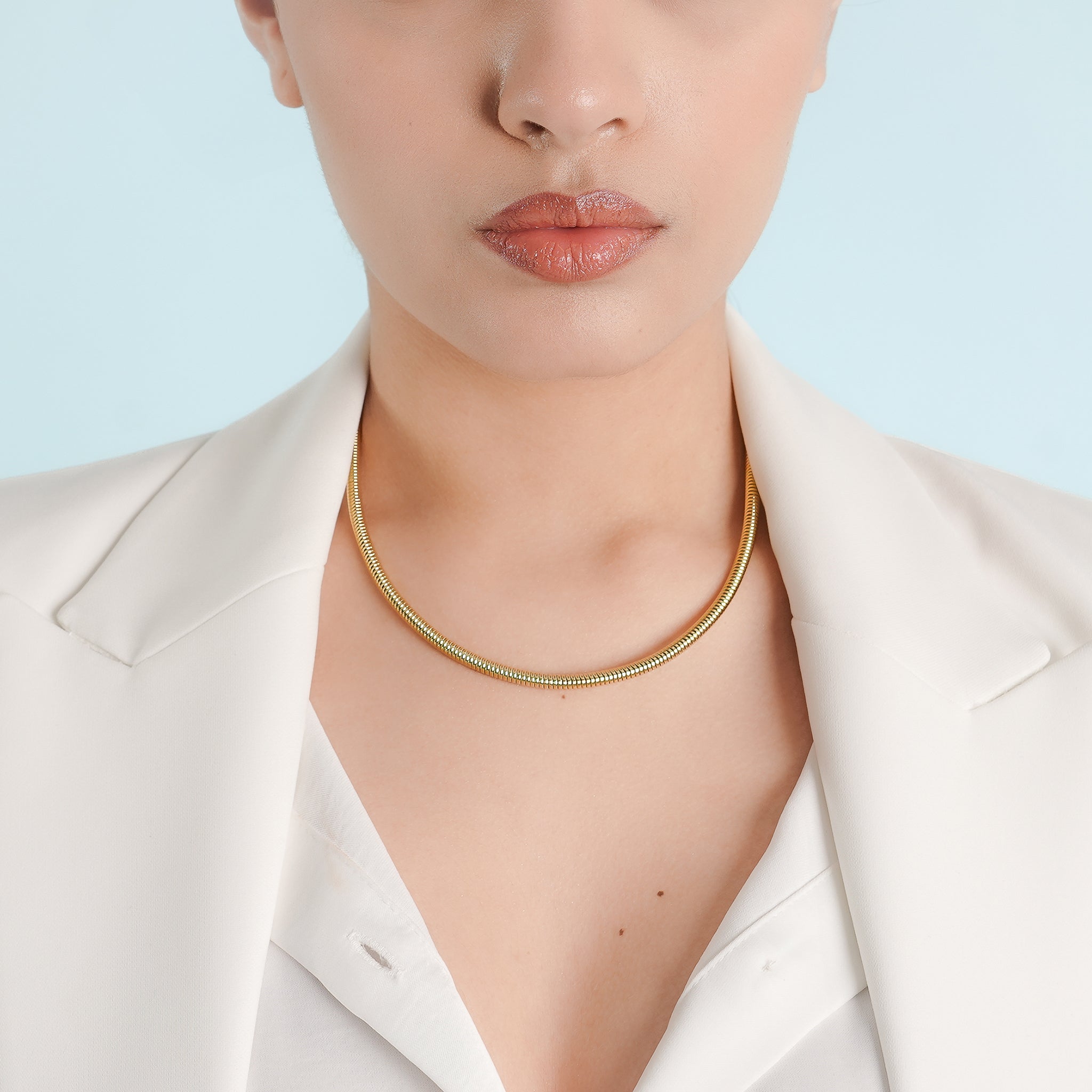 Model wearing an 18K gold snake chain necklace paired with a white blazer, highlighting its minimalist elegance on the neckline.