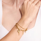 Gold bracelet with heart charm on a wrist against a light background