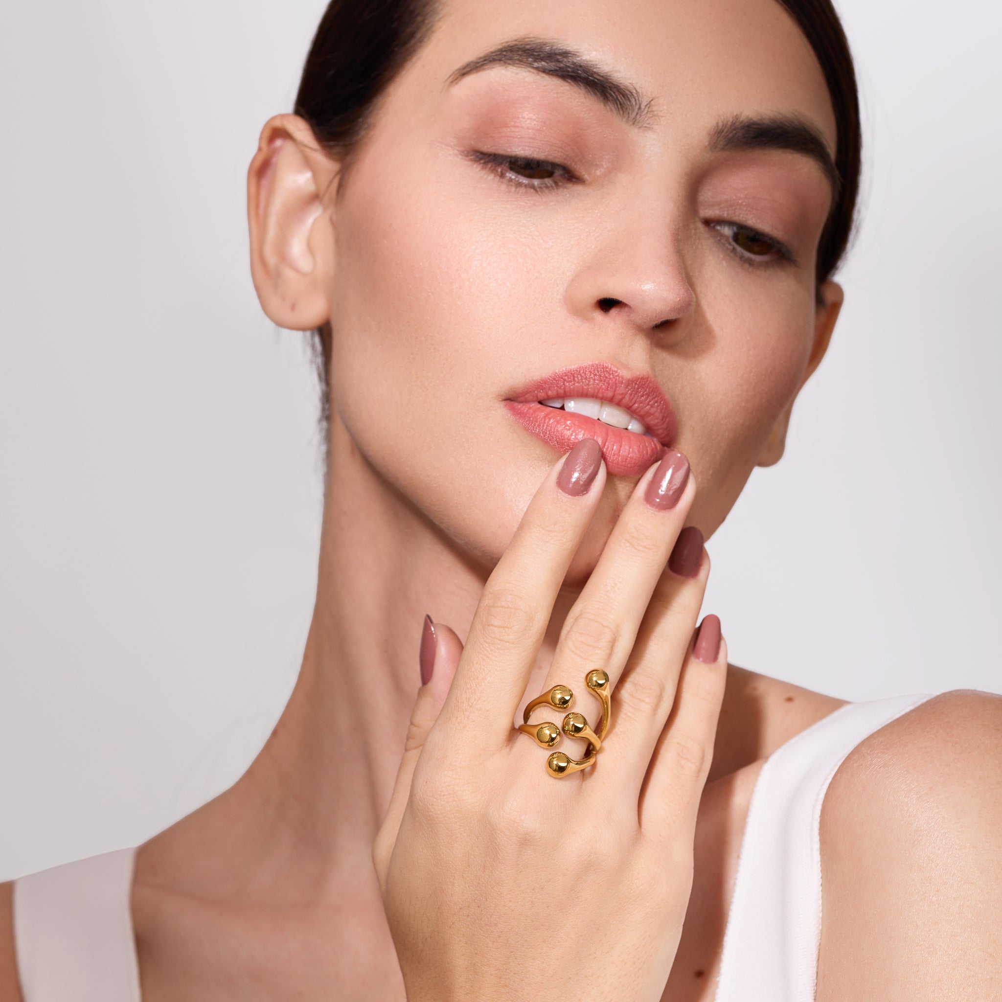 Woman wearing a gold ring on her finger against a plain background