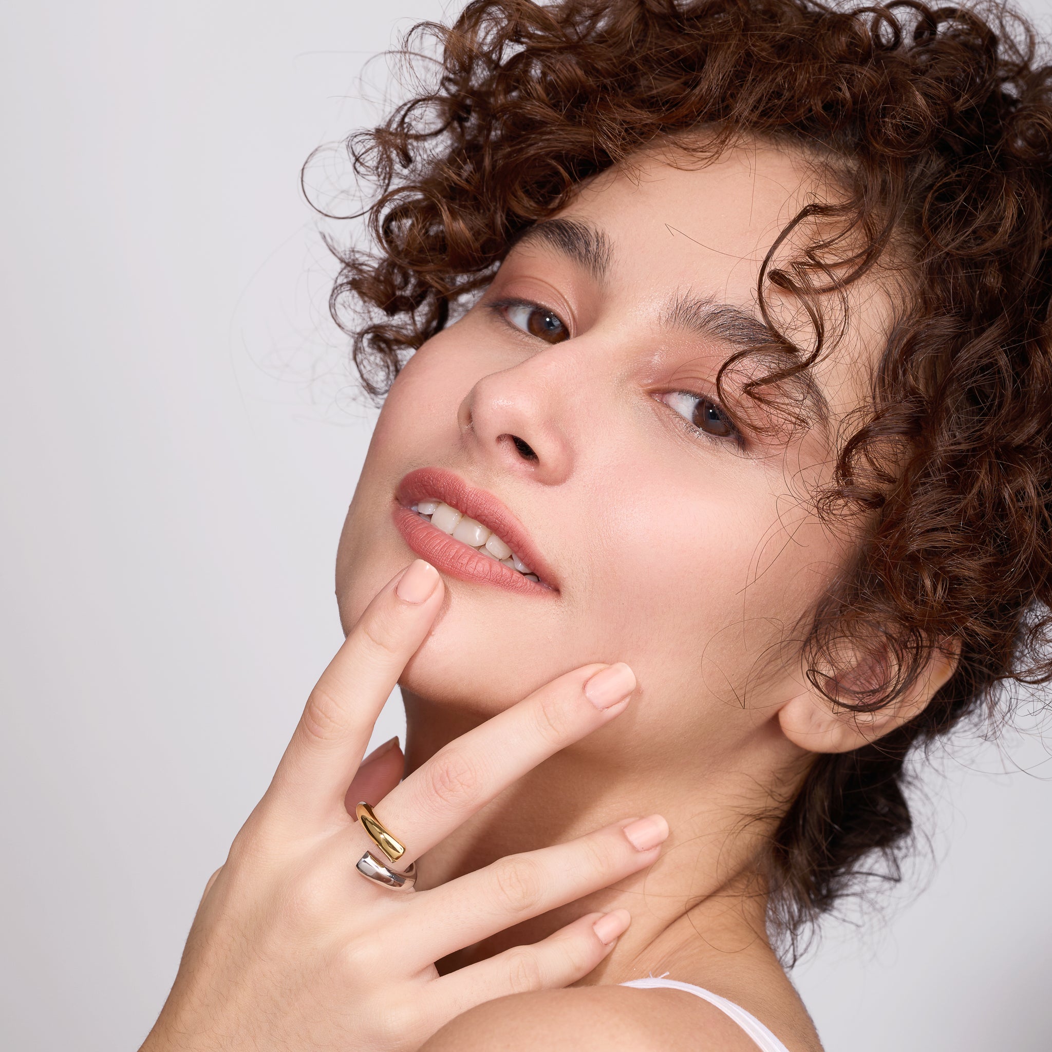 Woman with curly hair wearing two toned ring against a plain background