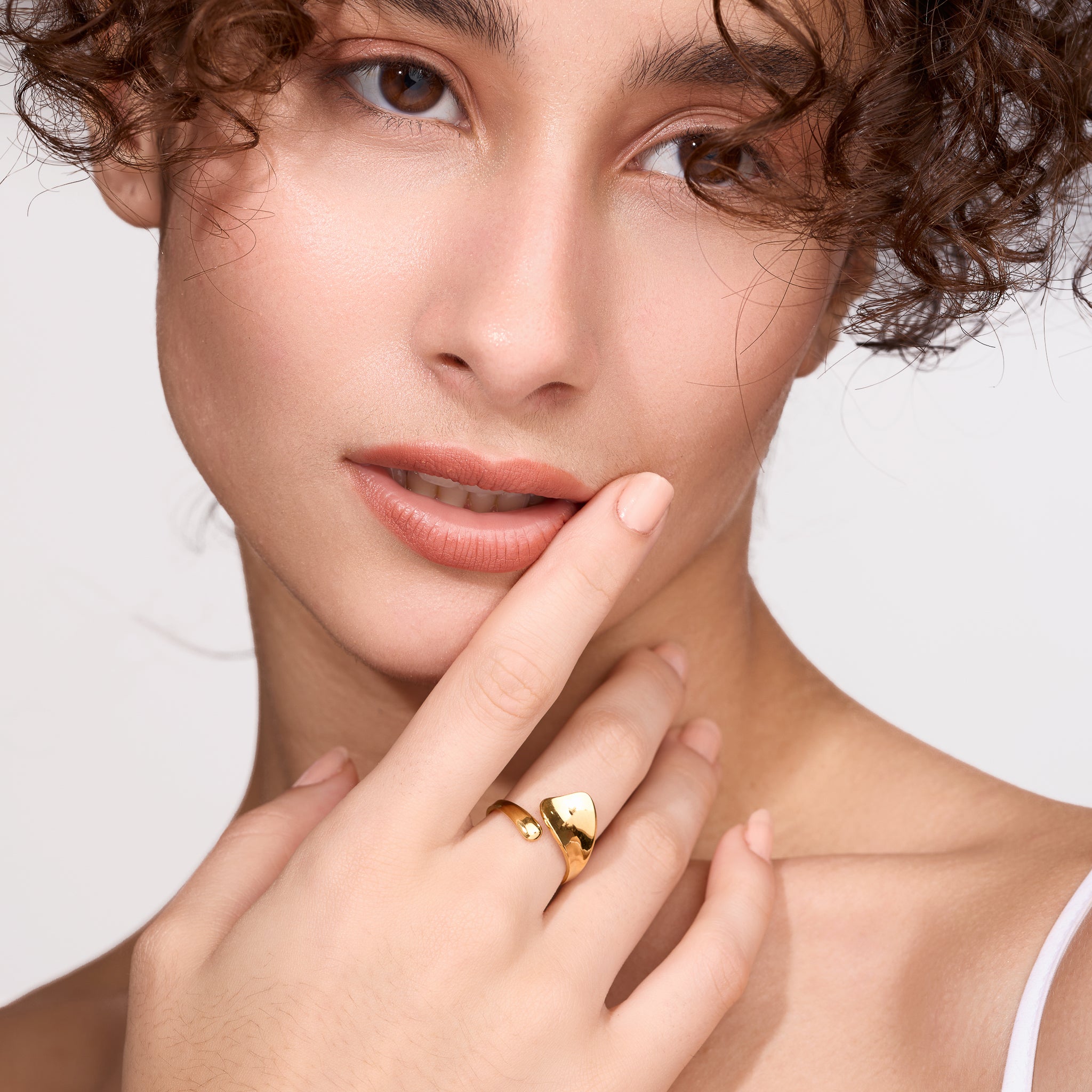 Close-up of a woman wearing a gold ring on a light background