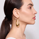 Woman wearing gold hoop earrings with a plain background