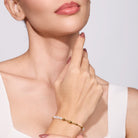 Close-up of a woman's hand wearing a gold bracelet with a pearl charm on a light background