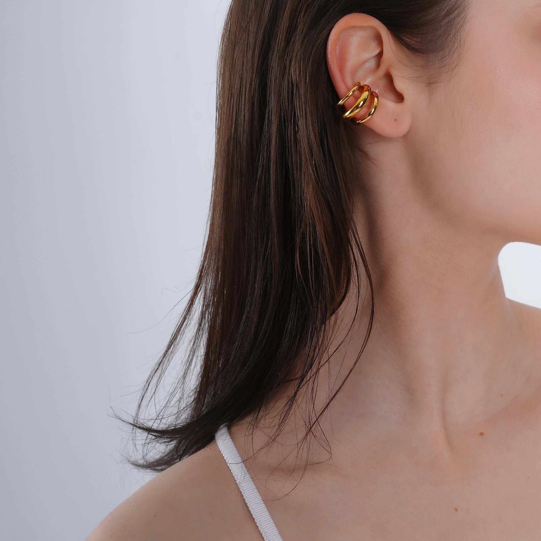 A model wearing 18K gold-plated triple-hoop ear cuffs, the layered hoops elegantly hugging the ear, adding a bold yet refined accent to the look.