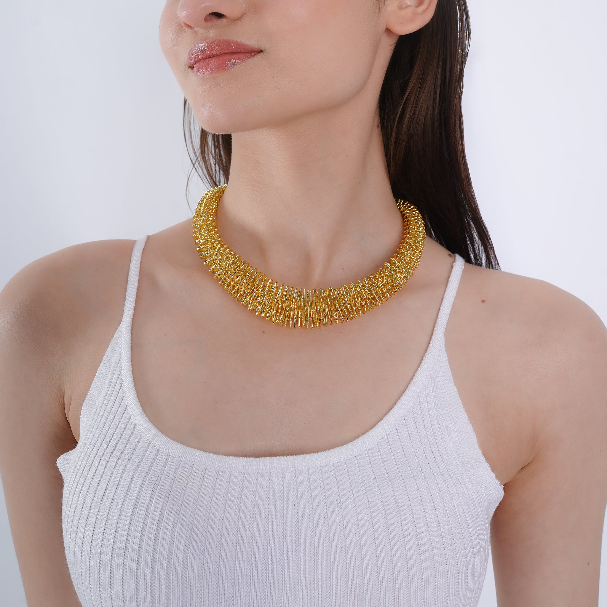 Model wearing an 18K gold-plated statement necklace with a textured, layered design, enhancing a chic neckline.
