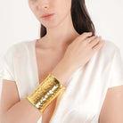 A model wearing the bold, hammered gold cuff bracelet on her wrist, complementing her elegant white outfit.