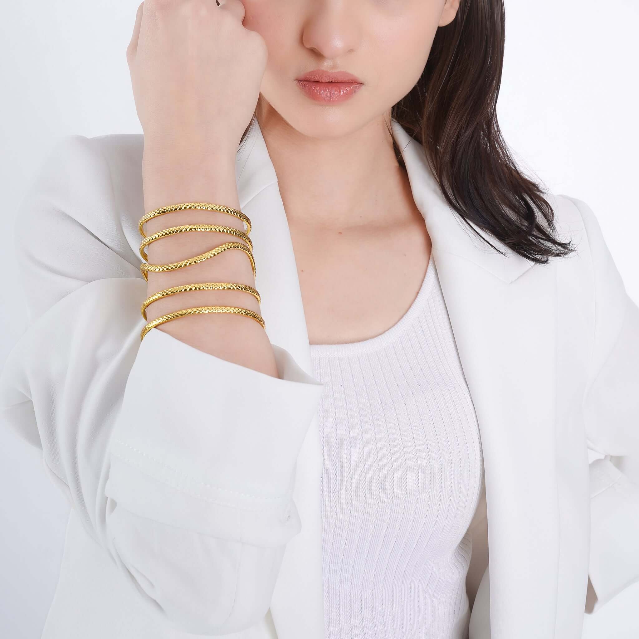 Woman wearing a stylish gold-plated interwoven cuff bracelet, highlighting its textured loops and radiant shine, complementing her white outfit for an elegant and sophisticated look.