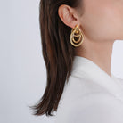 Side view of a model wearing the 18K gold-plated interlocking ring earrings, complementing her sleek hair and minimalist white outfit for a sophisticated look.