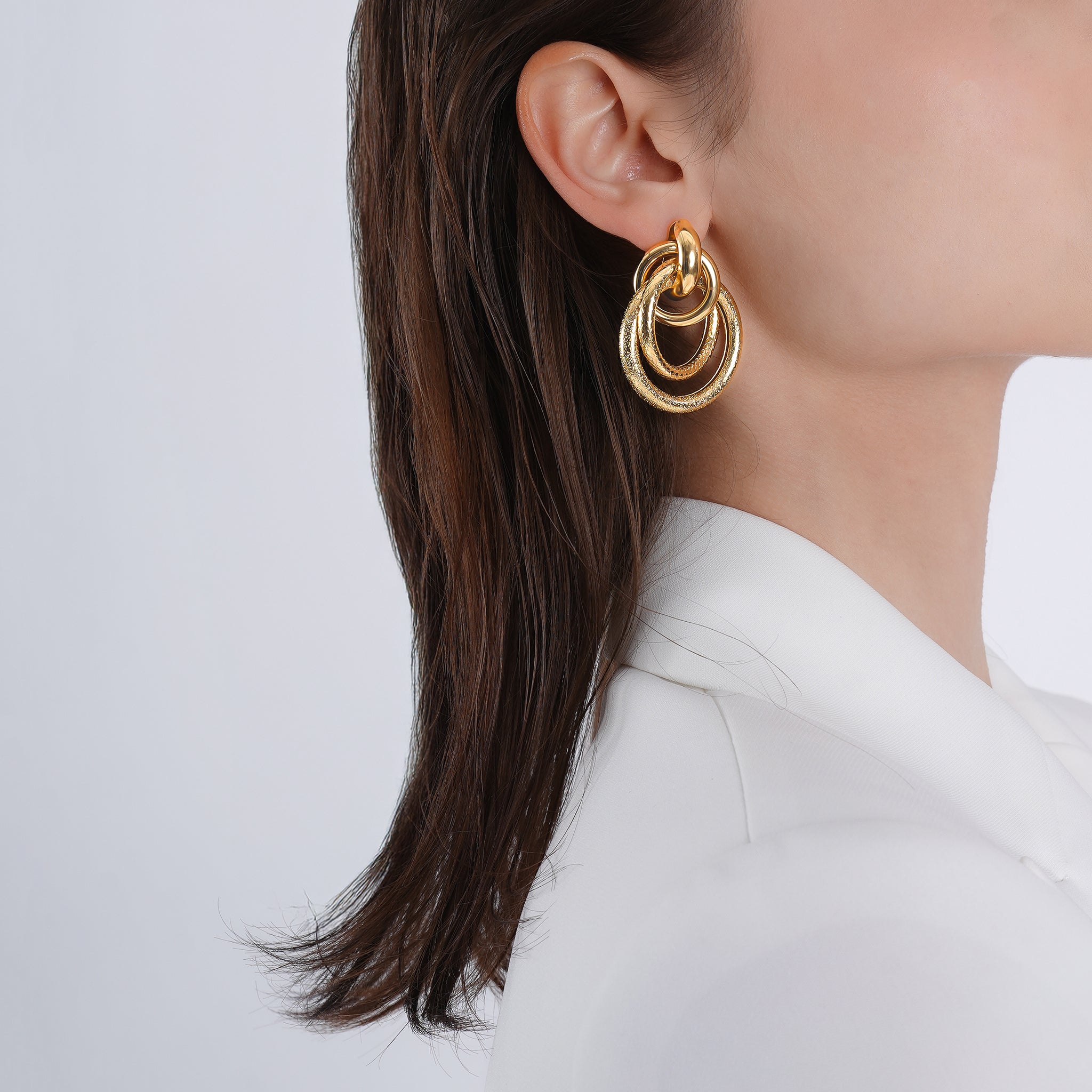 Side view of a model wearing the 18K gold-plated interlocking ring earrings, complementing her sleek hair and minimalist white outfit for a sophisticated look.