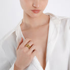 A model wearing the 18K gold-plated intertwined ring on the index finger, paired with a white silk blouse, enhancing its luxurious and sophisticated appeal.